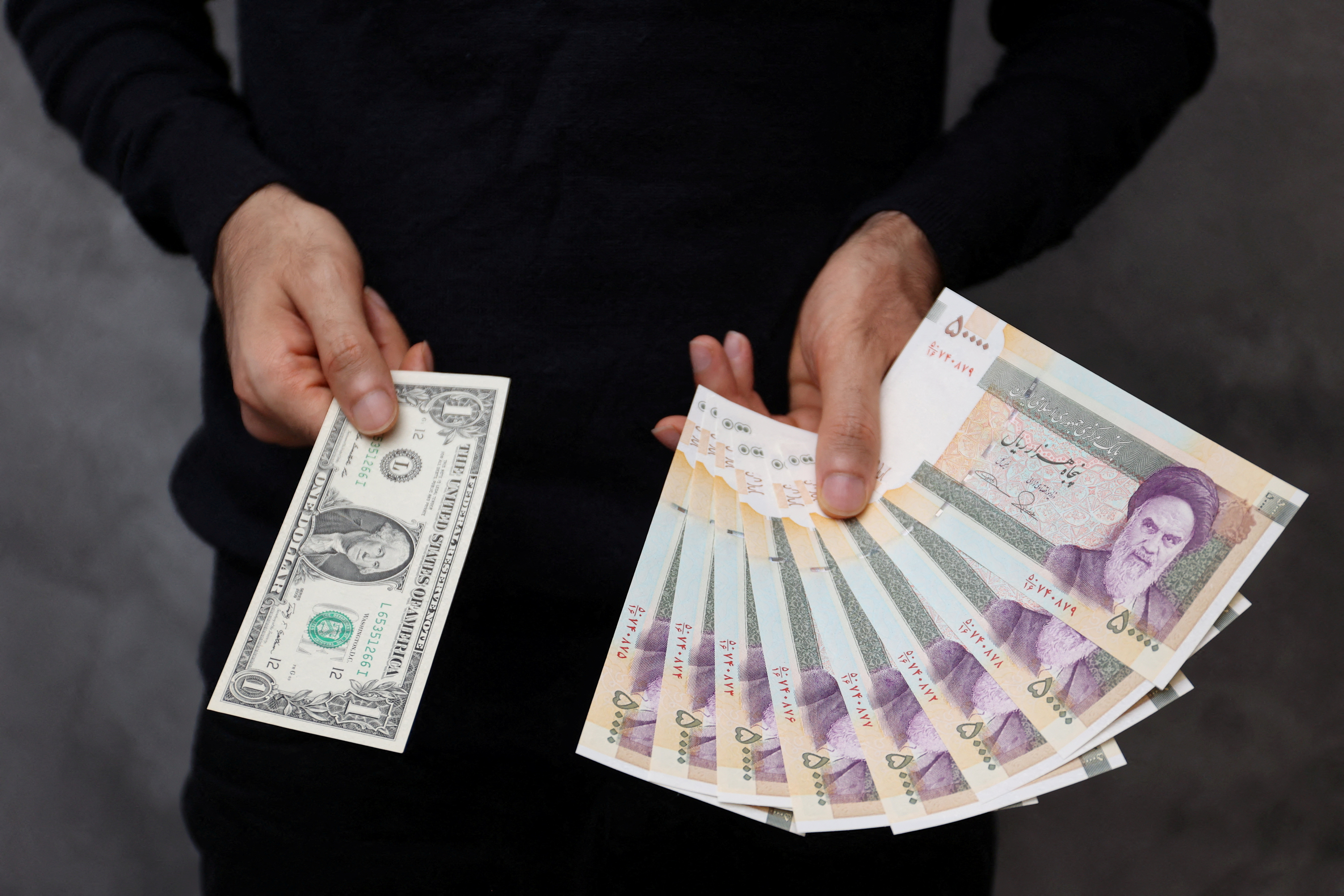 Un operador de divisas tiene dólares estadounidenses y riales iraníes en una tienda de cambio en Teherán