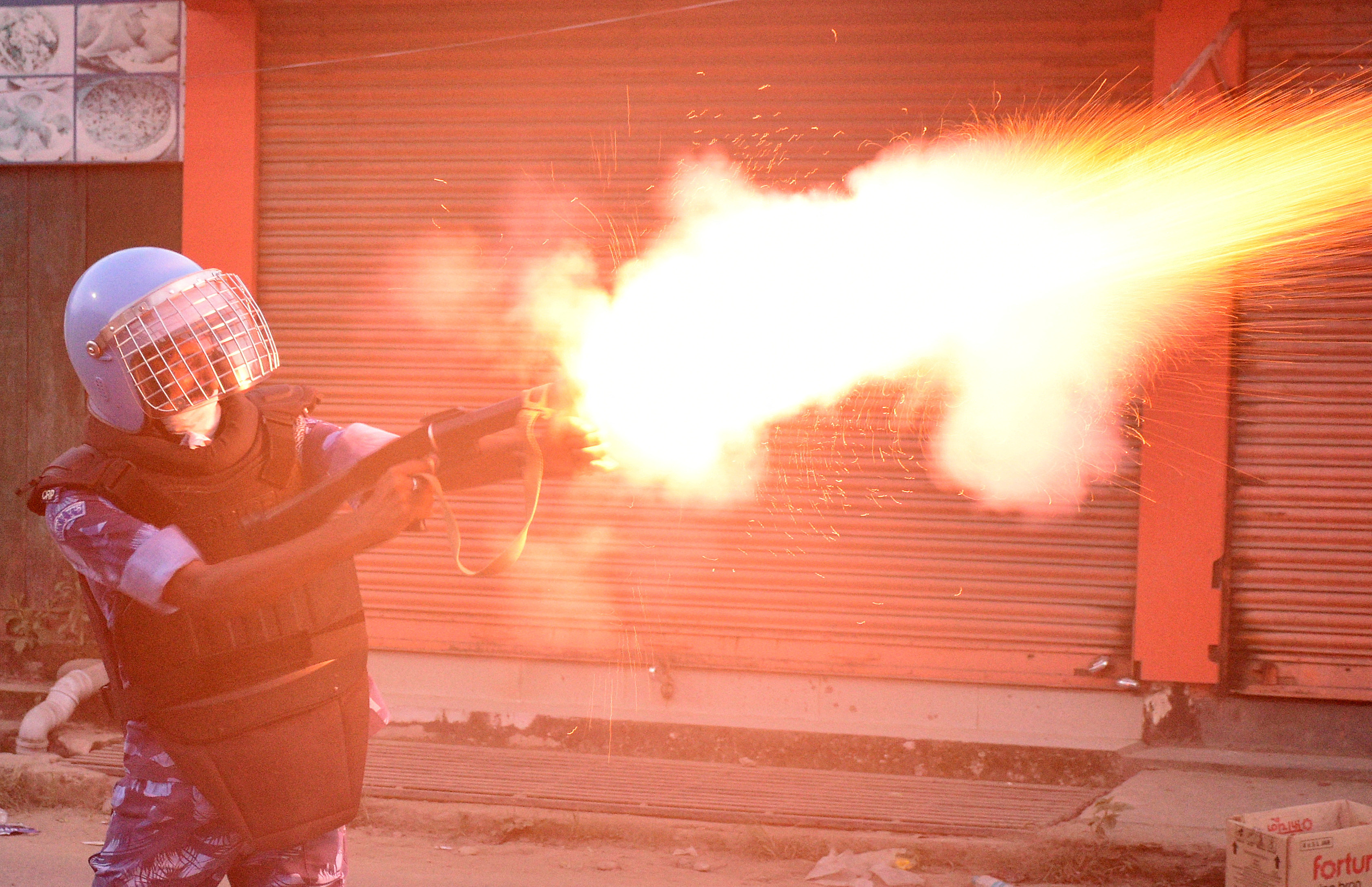 A riot police officer fires a tear smoke shell to disperse demonstrators, in Imphal