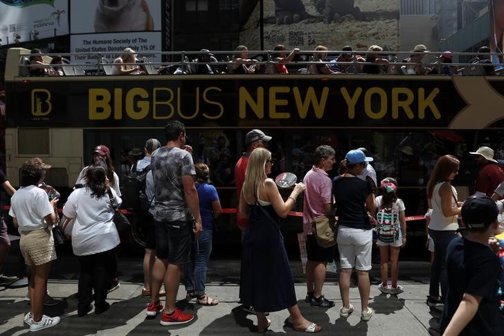 People wait in line to board an open-top city sightseeing tour bus while other sit seated at Times Square in New York