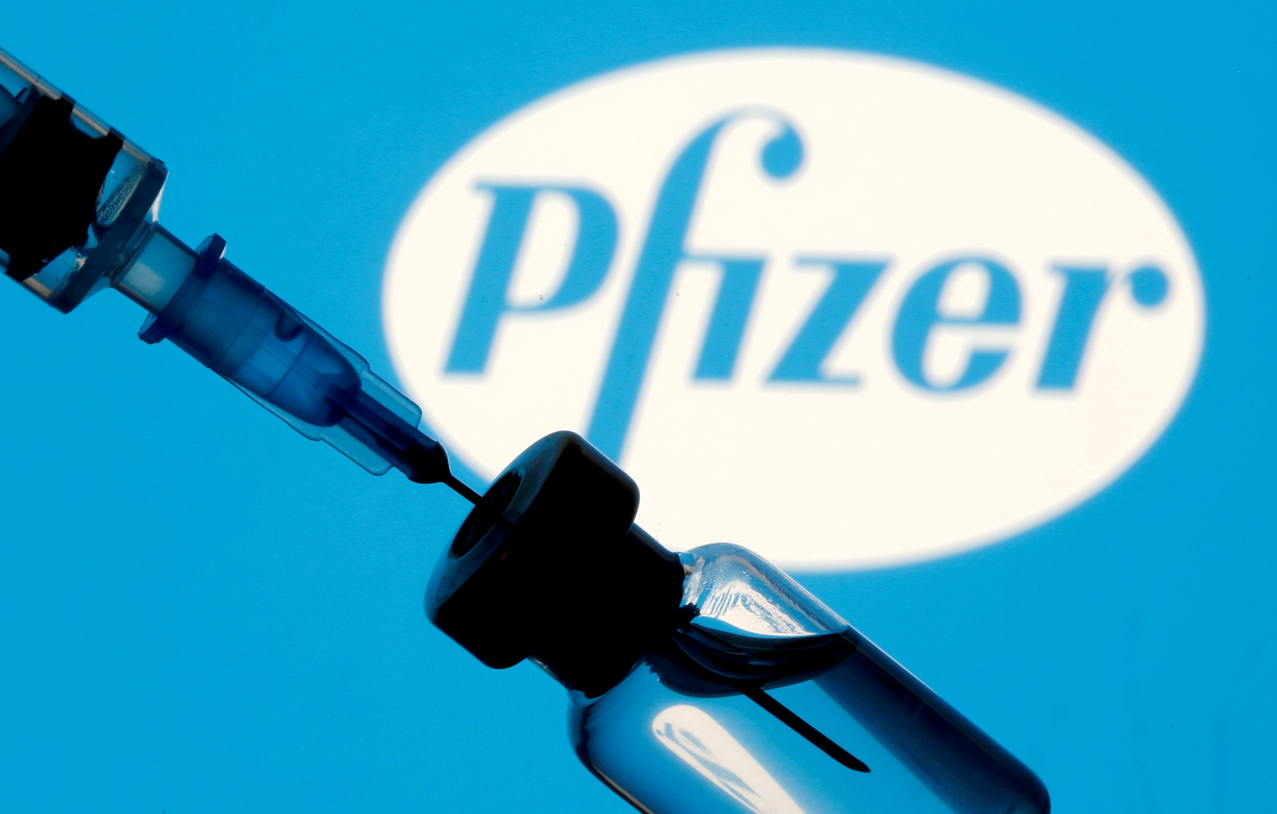 Vial and syringe are seen in front of displayed Pfizer logo