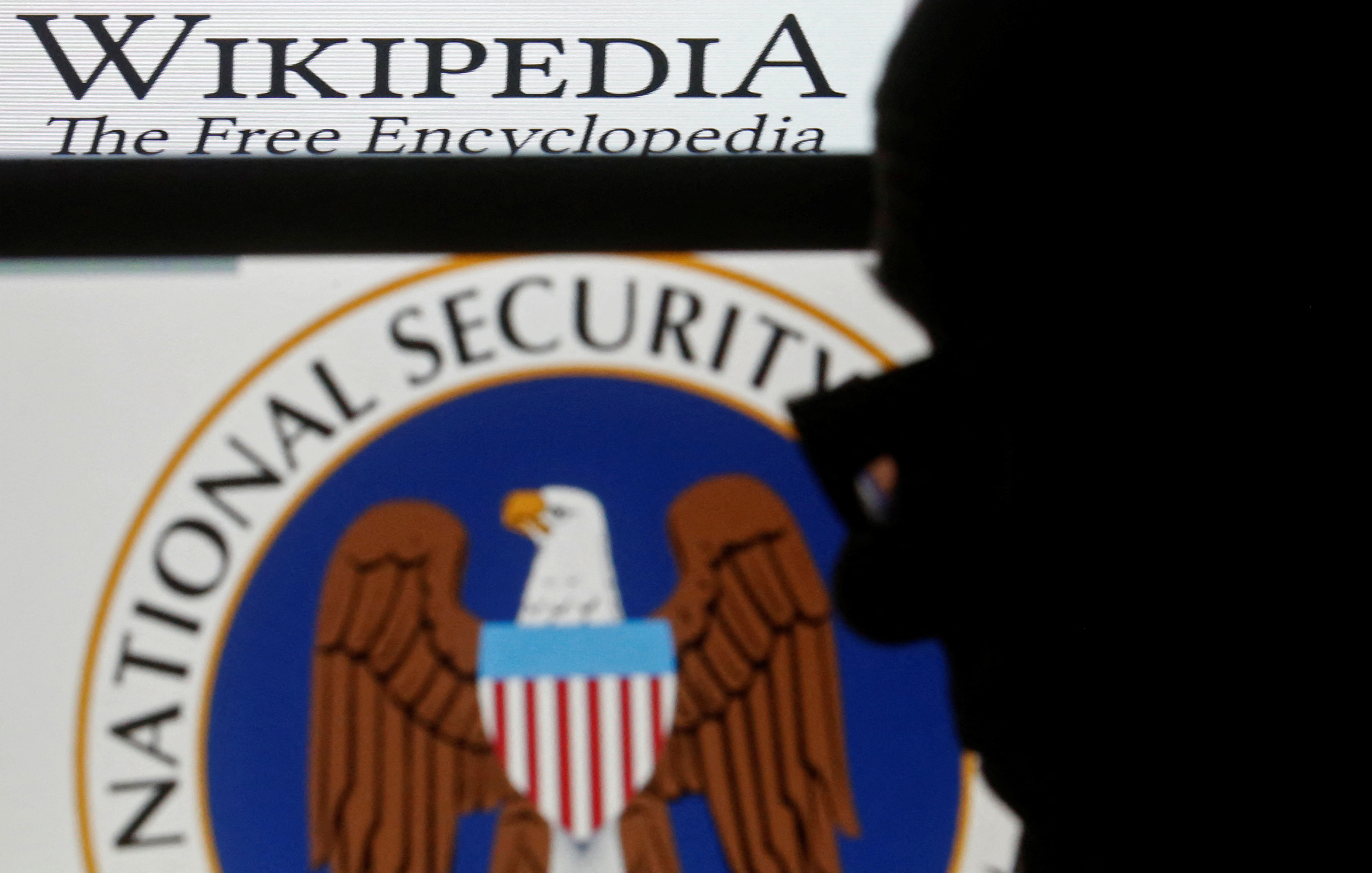 A man is silhouetted near logos of the U.S. National Security Agency (NSA) and Wikipedia in this photo illustration taken in Sarajevo