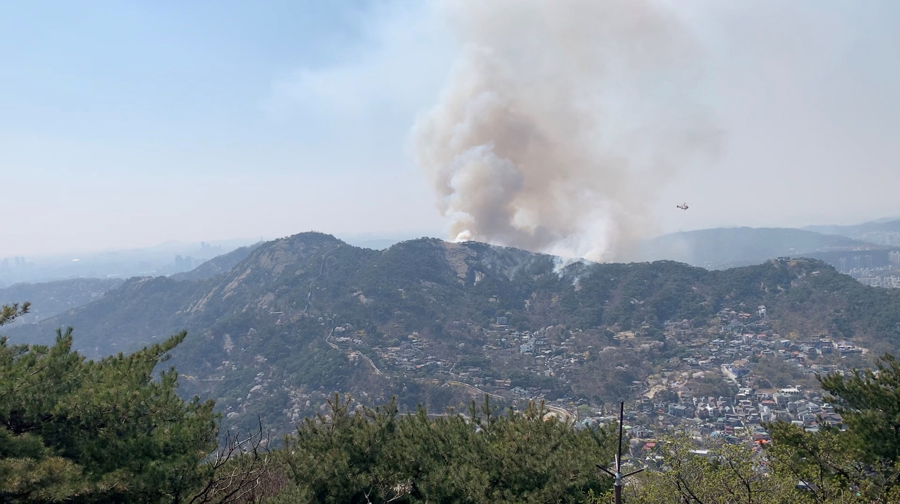 A helicopter flies past a smoke emerging on Inwangsan mountain, in Seoul
