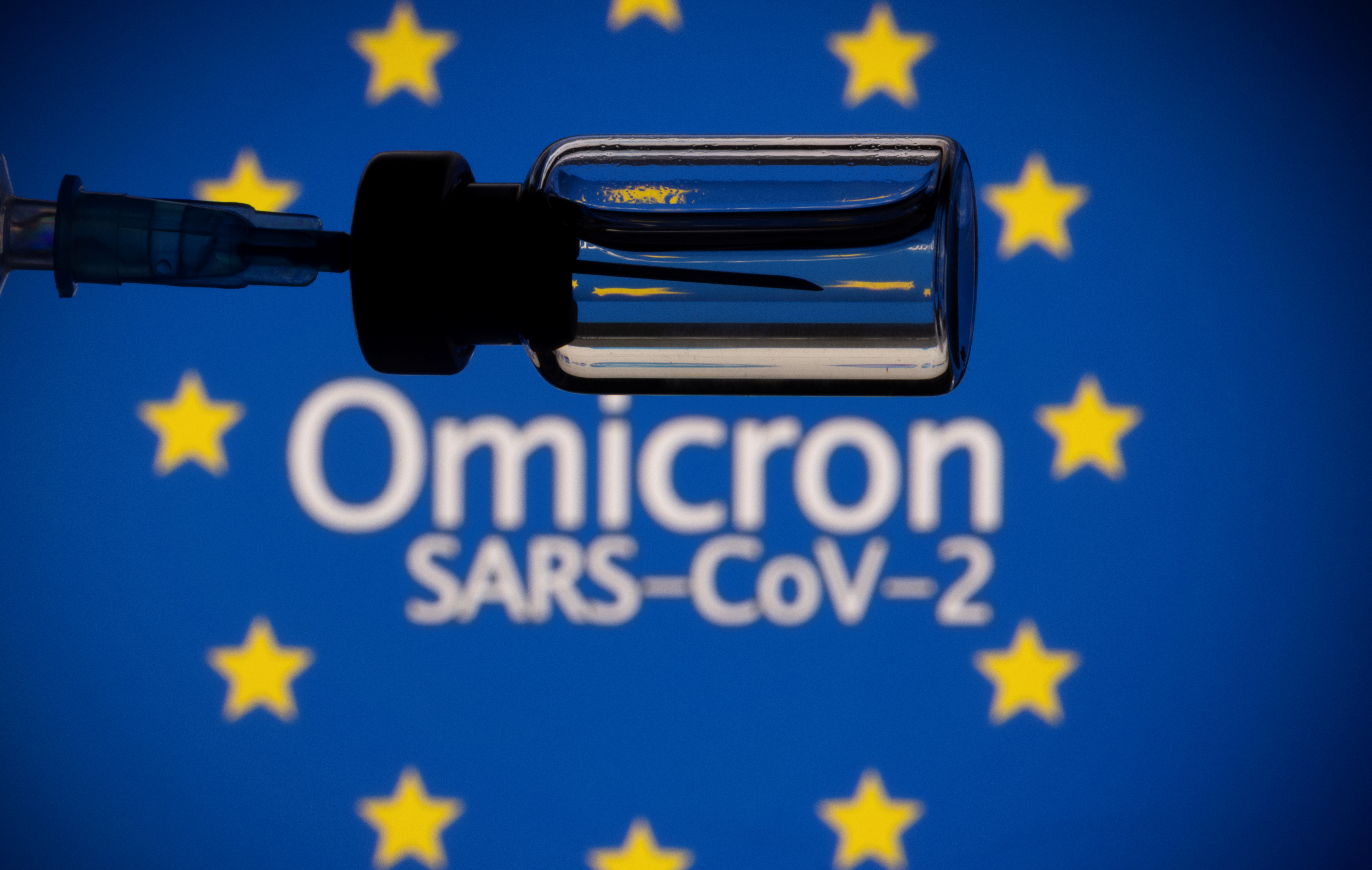 A vial and a syringe are seen in front of a displayed EU flag and words "Omicron SARS-CoV-2" in this illustration taken