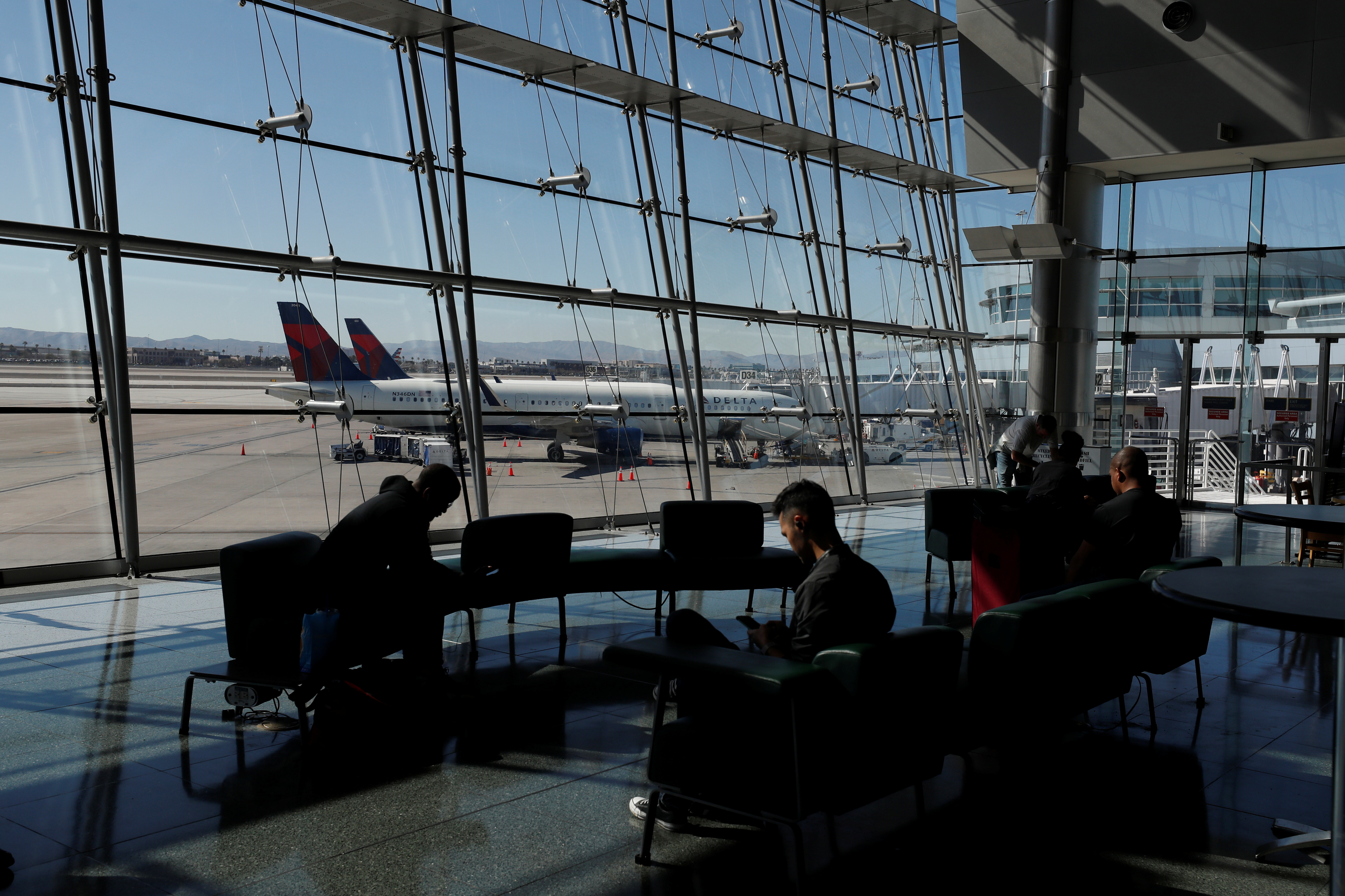 Travelers sit in a lounge area as Delta Air Lines plane park at a gate in McCarran International Airport in Las Vegas