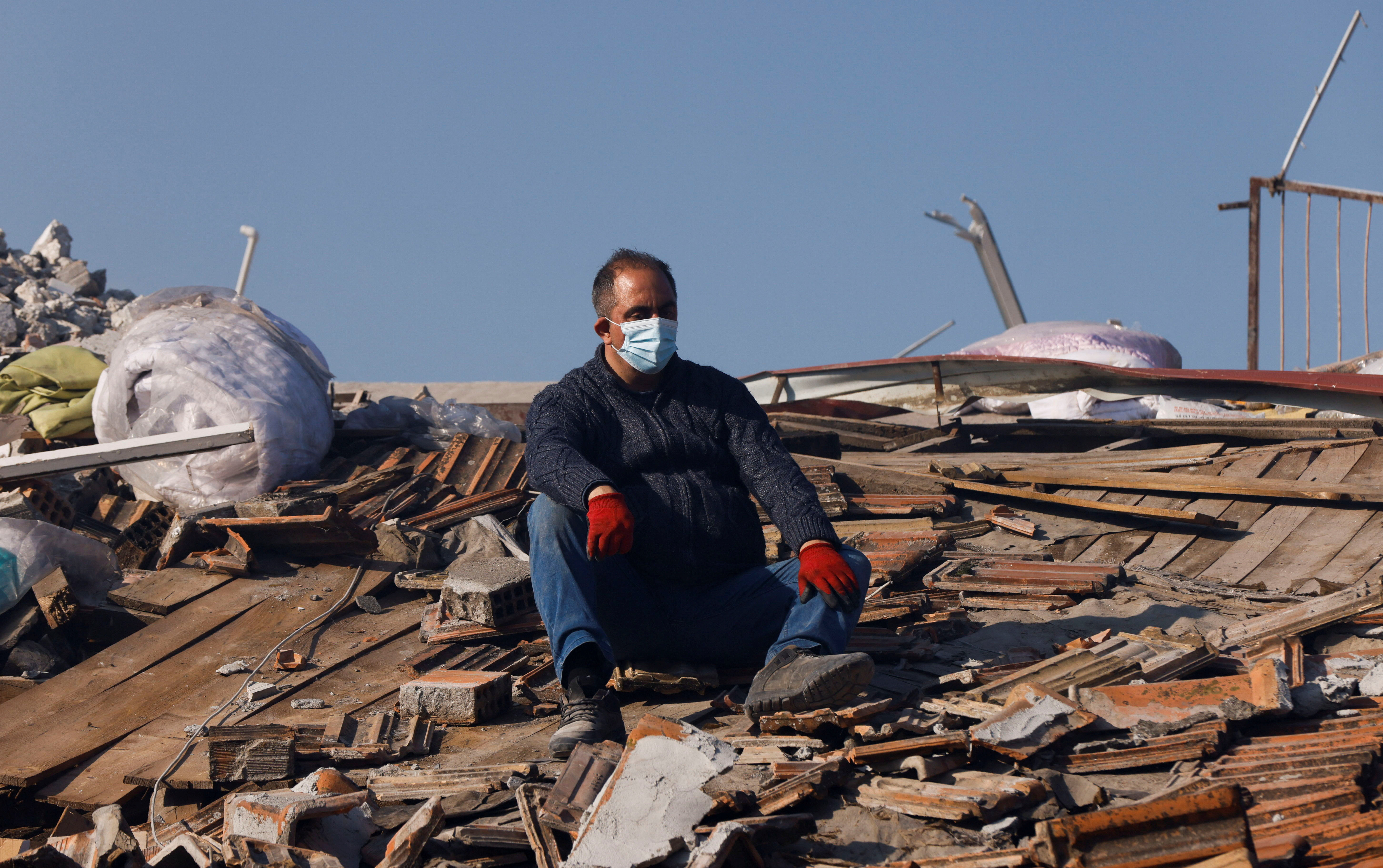 A man sits on what is left of a roof surrounded by rubble following the earthquake in Hatay, Turkey