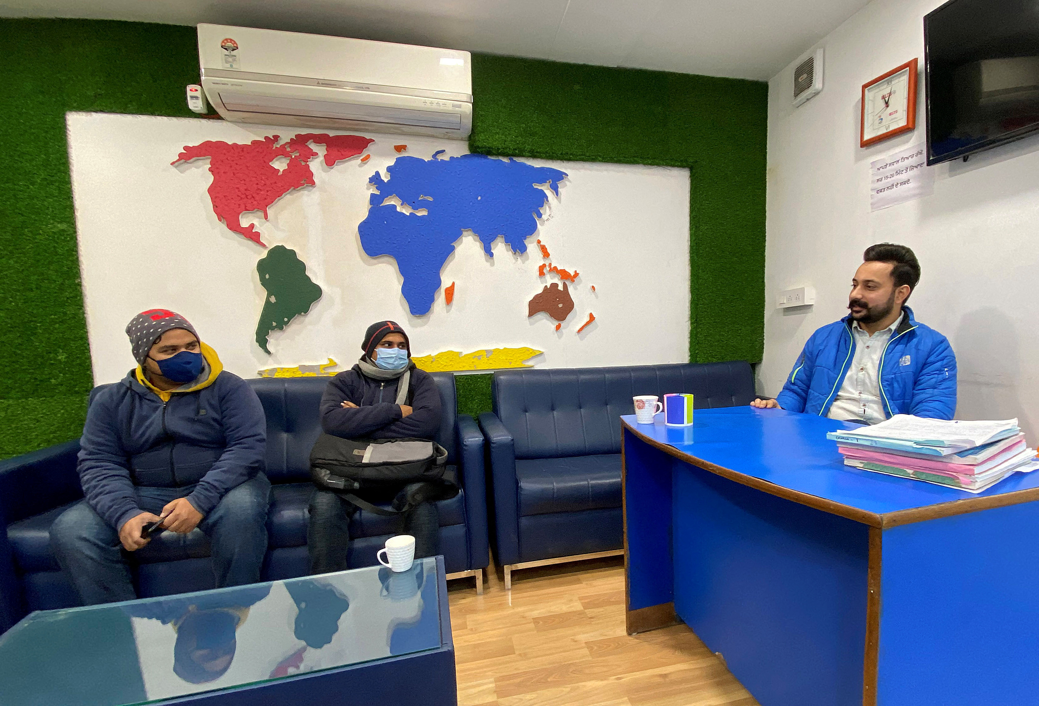 Srijan Upadhyay and Sagar Sharma from the eastern state of Bihar listen to Lovepreet, an immigration counsellor of Blue Line consultants, at his office in Rajpura