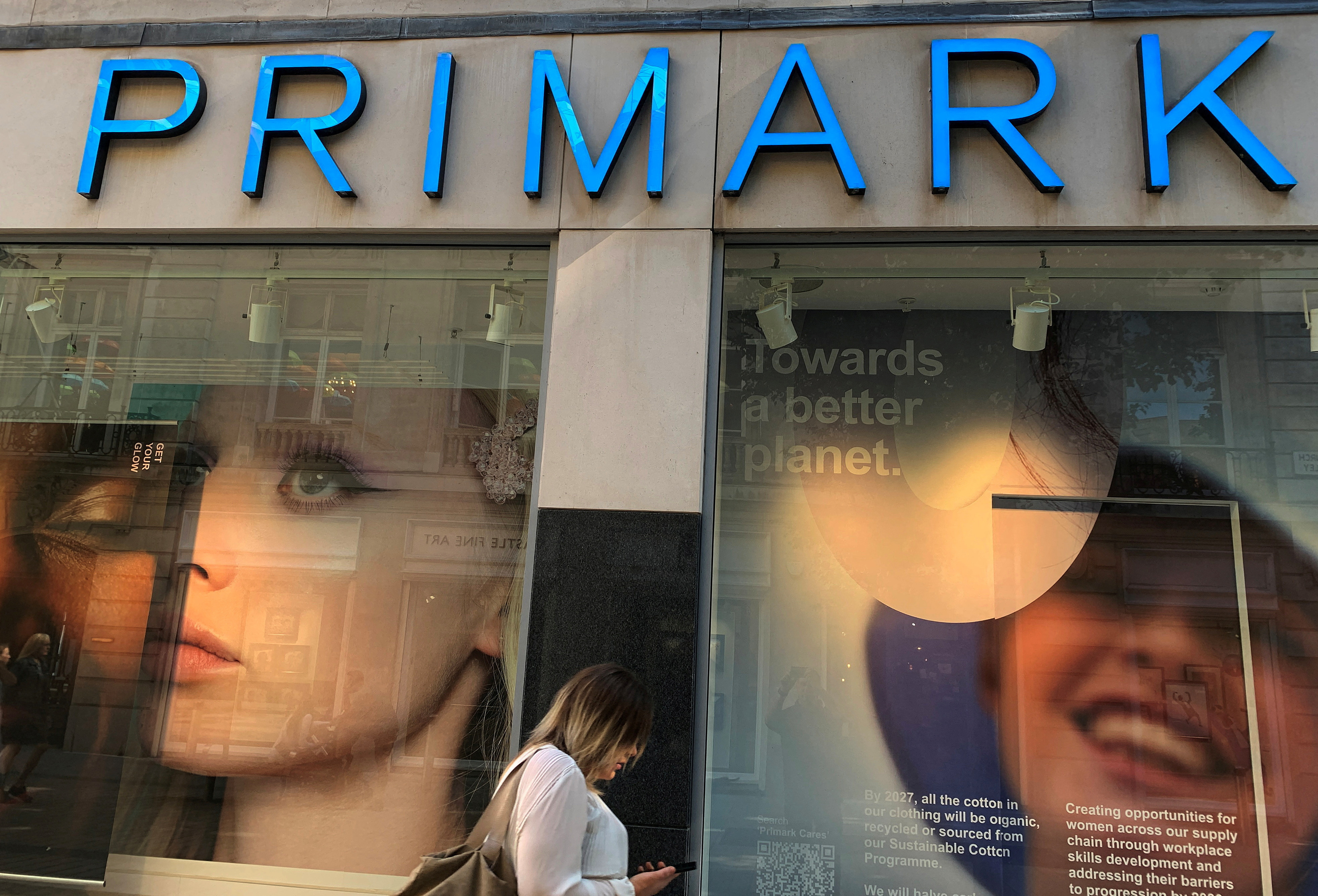 A woman walks past a window display showing new environmentally themed posters at a Primark store in Liverpool
