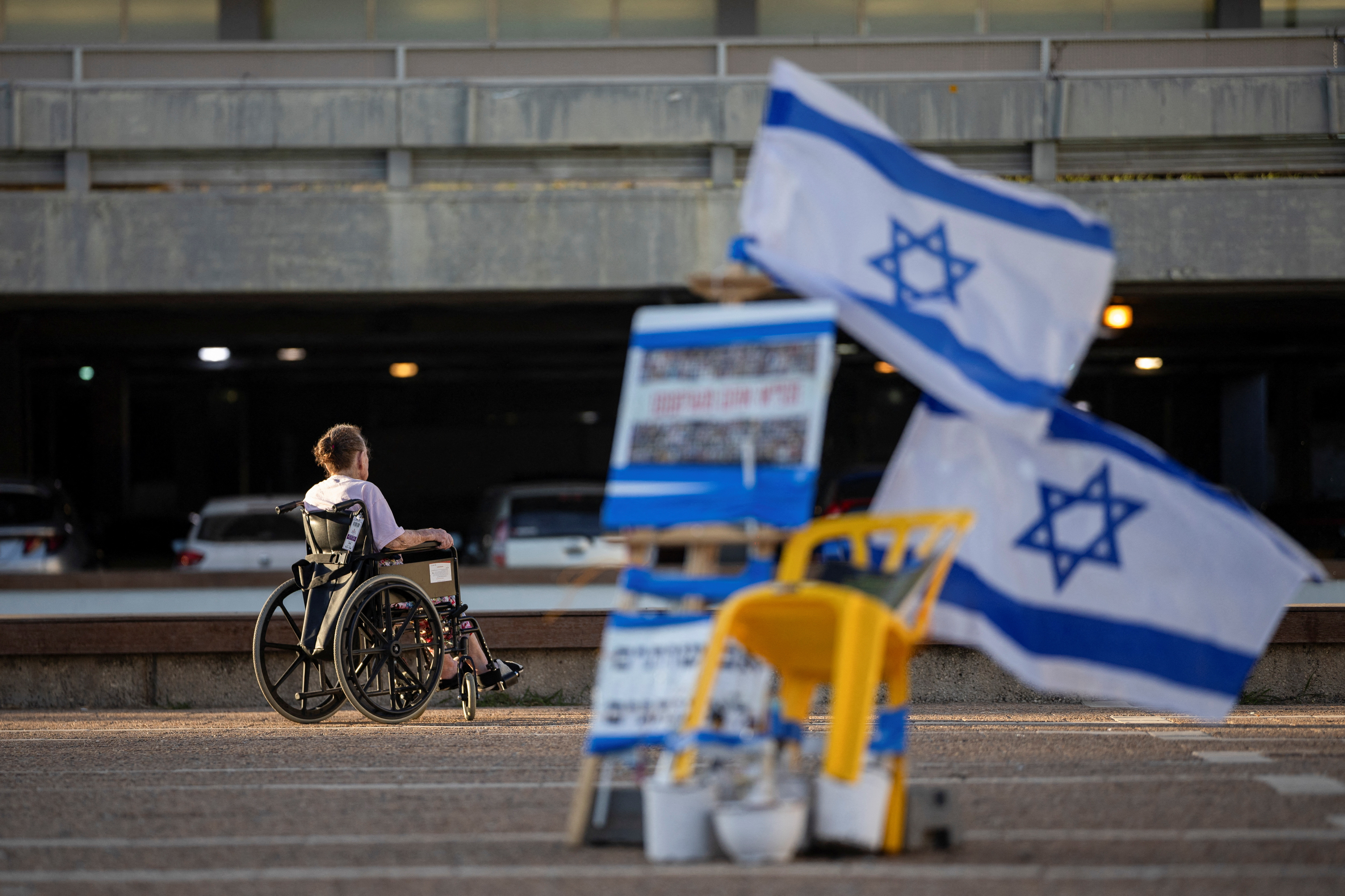 A man in a wheelchair passes near Israeli flags and pictures of hostages kidnapped during the deadly  October 7 attack by Hamas, in Tel Aviv