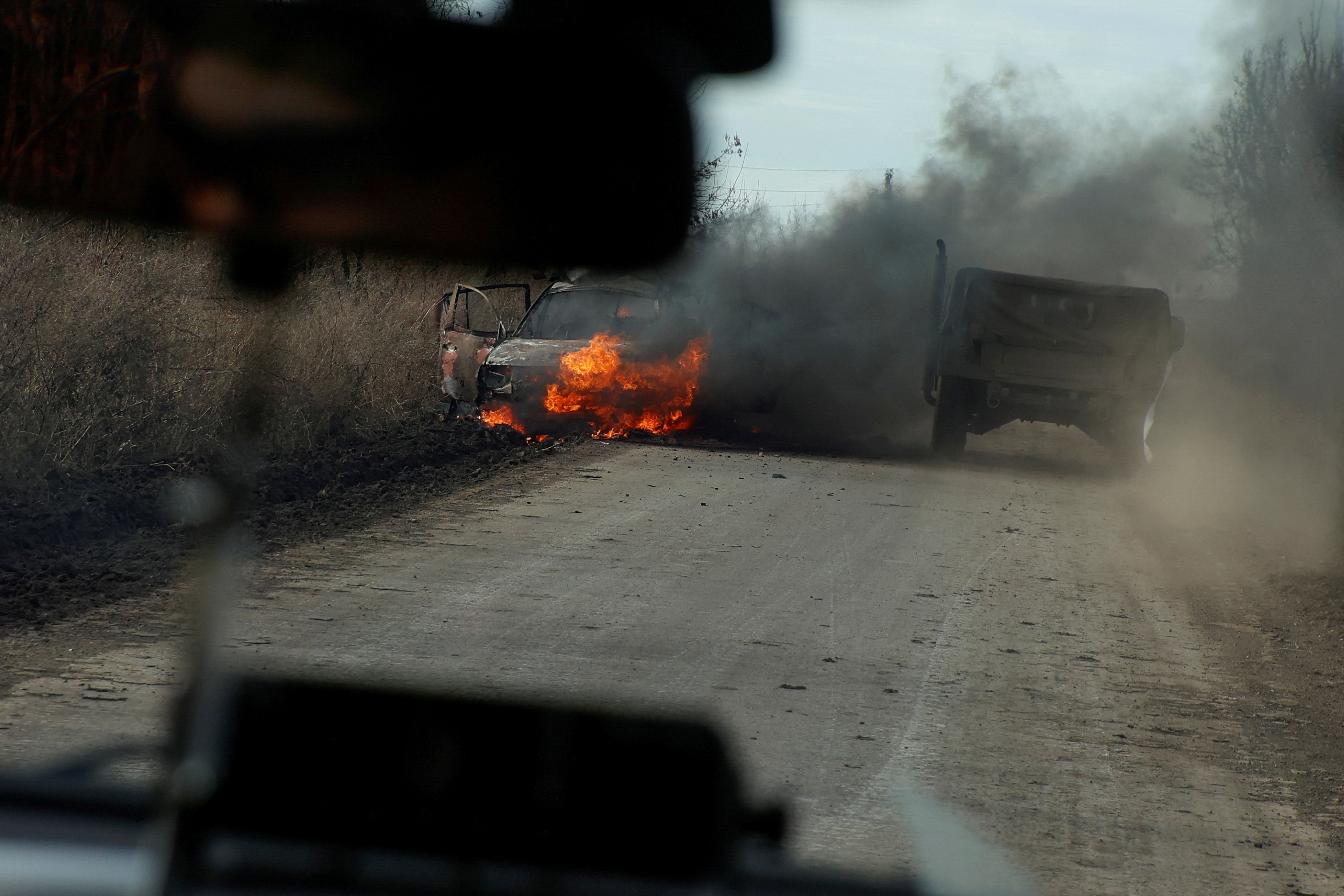 Ukrainian servicemen move past a burning car hit by a kamikaze drone outside the front line town of Avdiivka