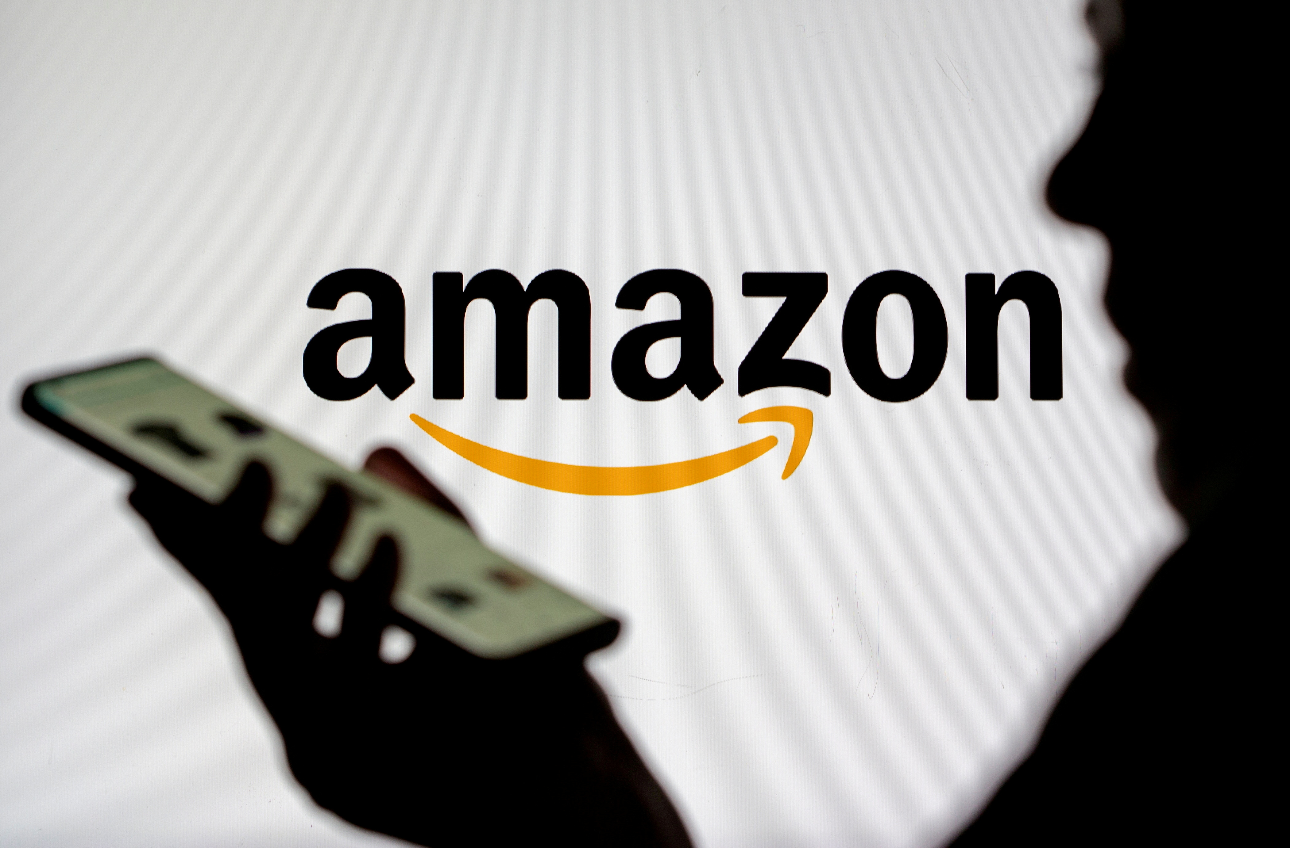 Woman with smartphone is seen in front of displayed Amazon logo in this illustration taken, July 30, 2021. REUTERS/Dado Ruvic/Illustration