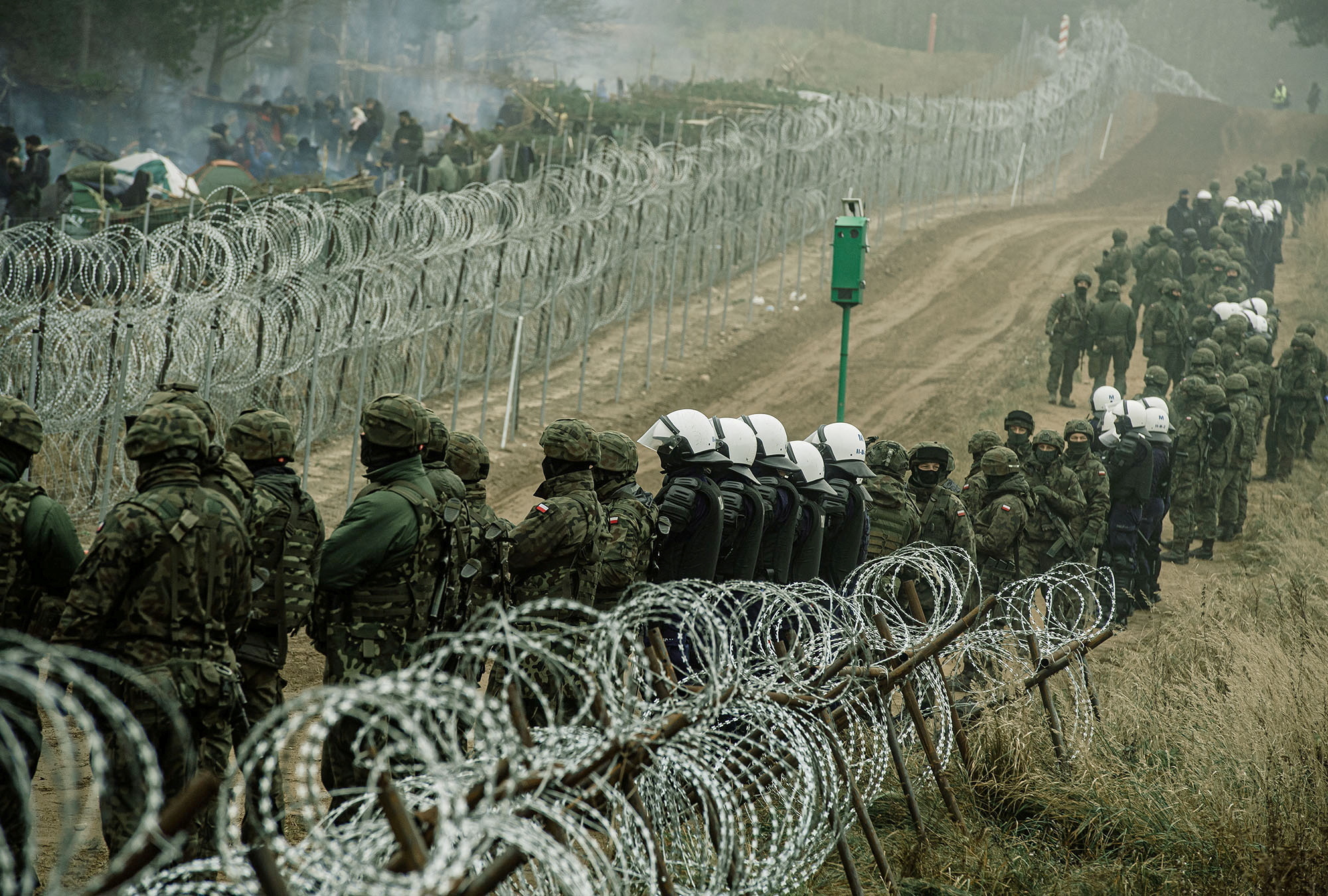 Polish soldiers and police watch migrants at the Poland/Belarus border near Kuznica, Poland, in this photograph released by the Territorial Defence Forces, November 12, 2021.  Irek Dorozanski/DWOT/Handout via REUTERS 