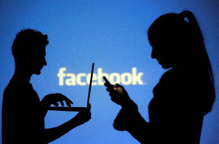 People pose with laptops in front of projection of Facebook logo in this picture illustration taken in Zenica