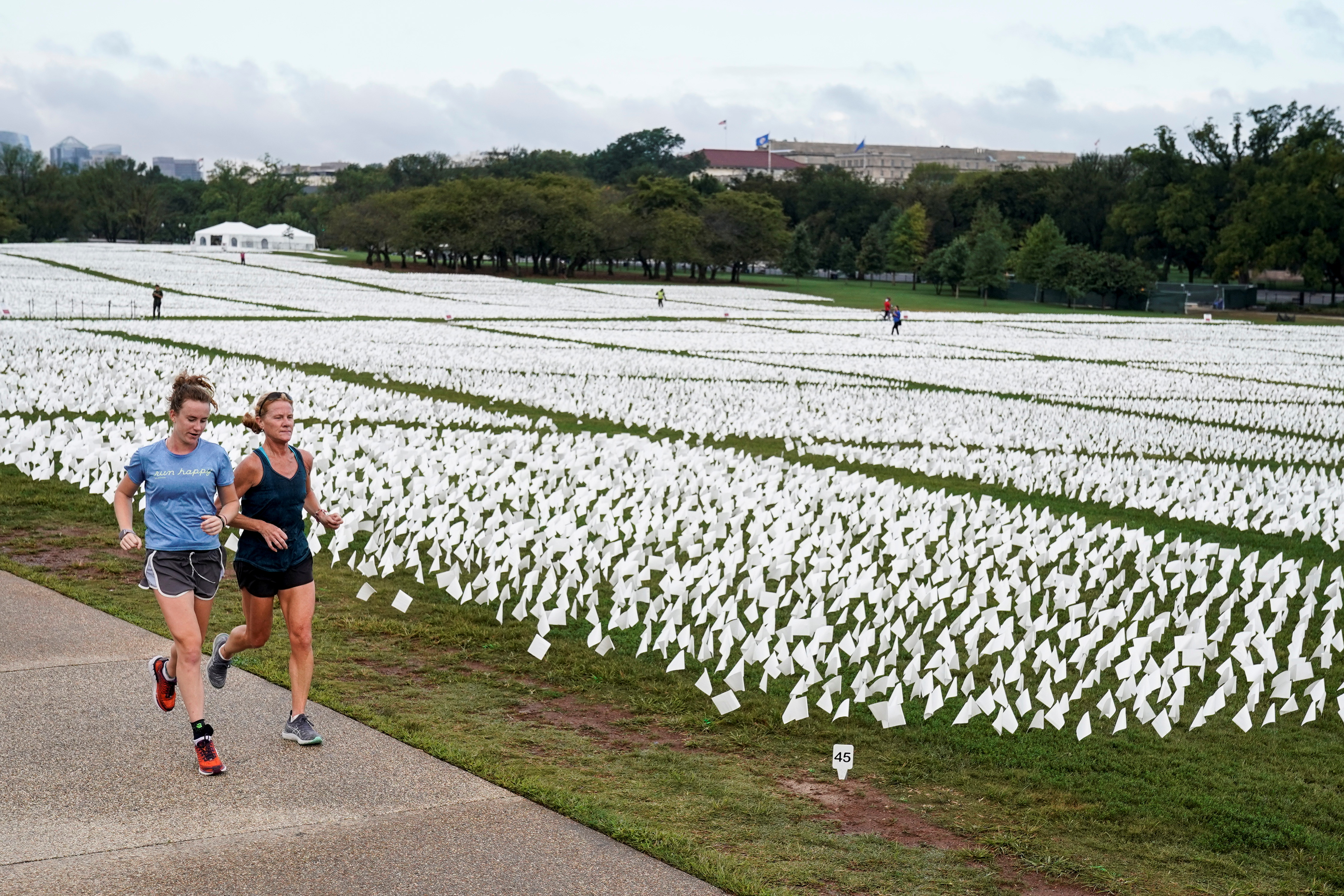 Women run past an exhibition of white flags representing Americans who have died of coronavirus disease (COVID-19), placed over 20 acres of the National Mall, in Washington, U.S., September 17, 2021.      REUTERS/Joshua Roberts