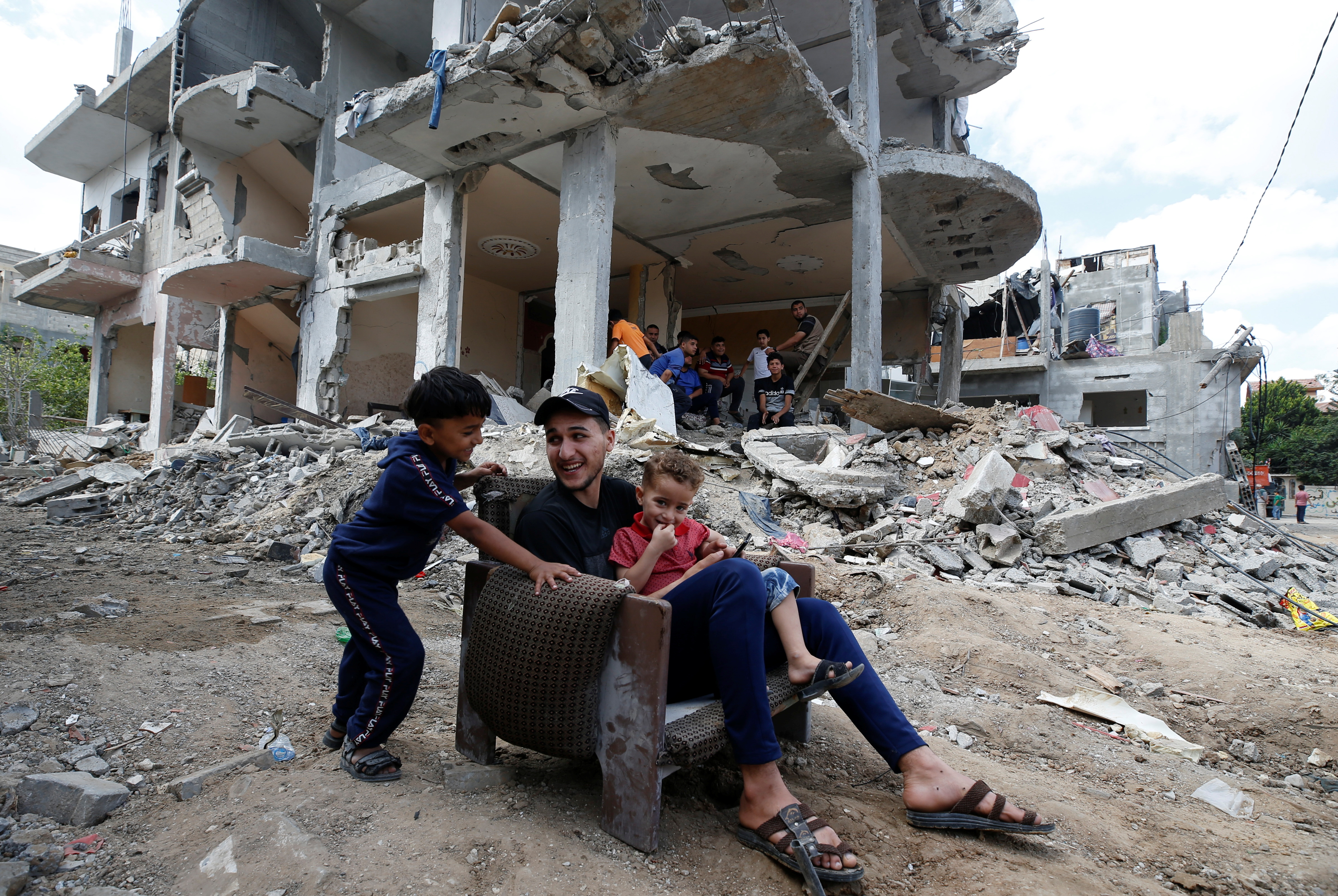 Palestiniečiai sėdi ant kėdės pastato griuvėsiuose, kurie buvo apgadinti Izraelio oro smūgiuose per Izraelio ir „Hamas“ kovas Gazoje 23 m. Gegužės 2021 d. REUTERS / Mohammed Salem