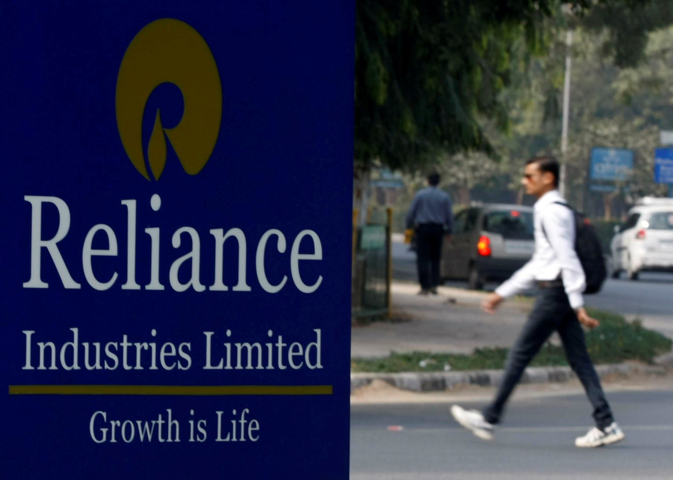 A man walks past a Reliance Industries Limited sign board installed on a road divider in Gandhinagar
