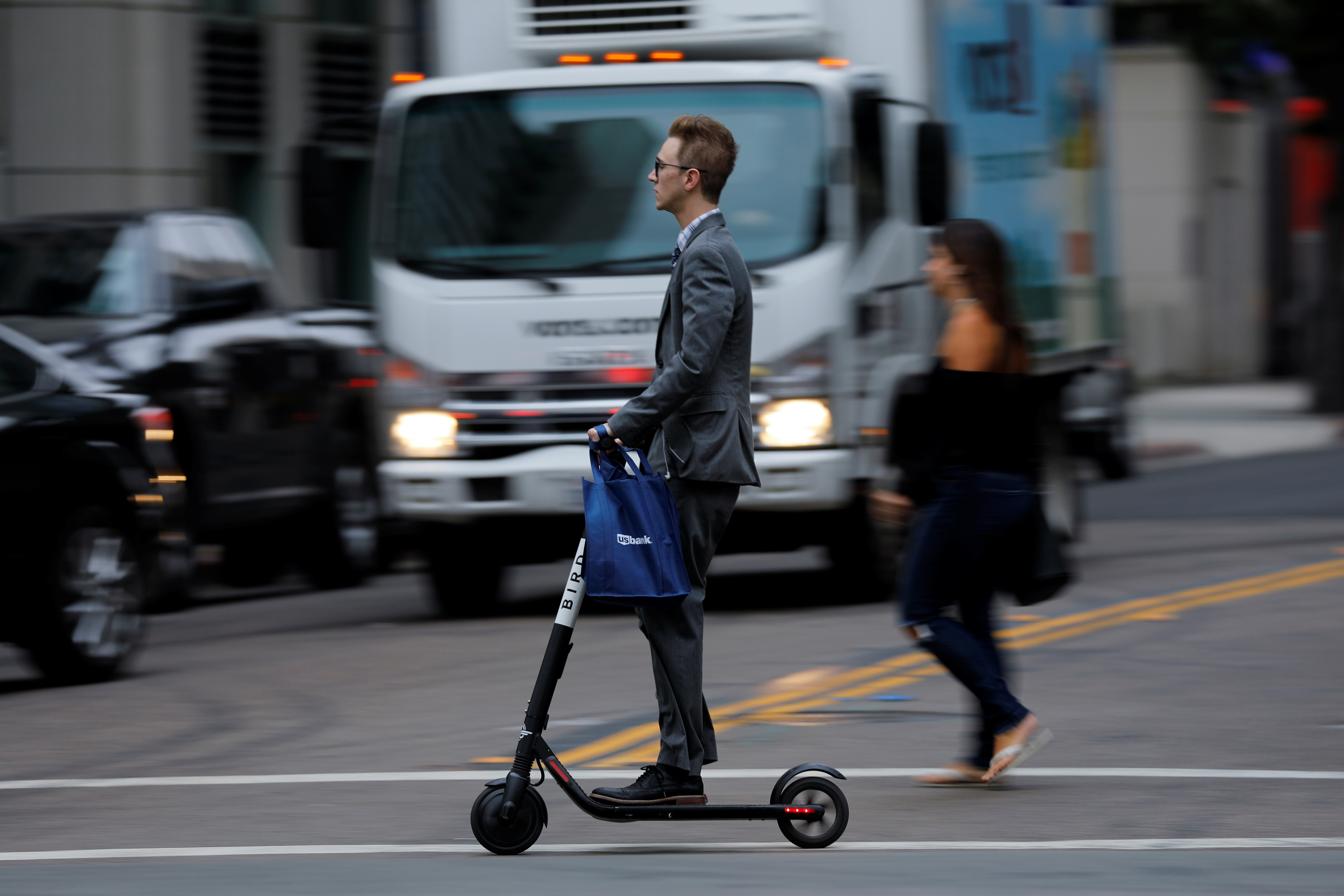 A man in a suit rides an electric BIRD rental scooter along a city street in San Diego, California