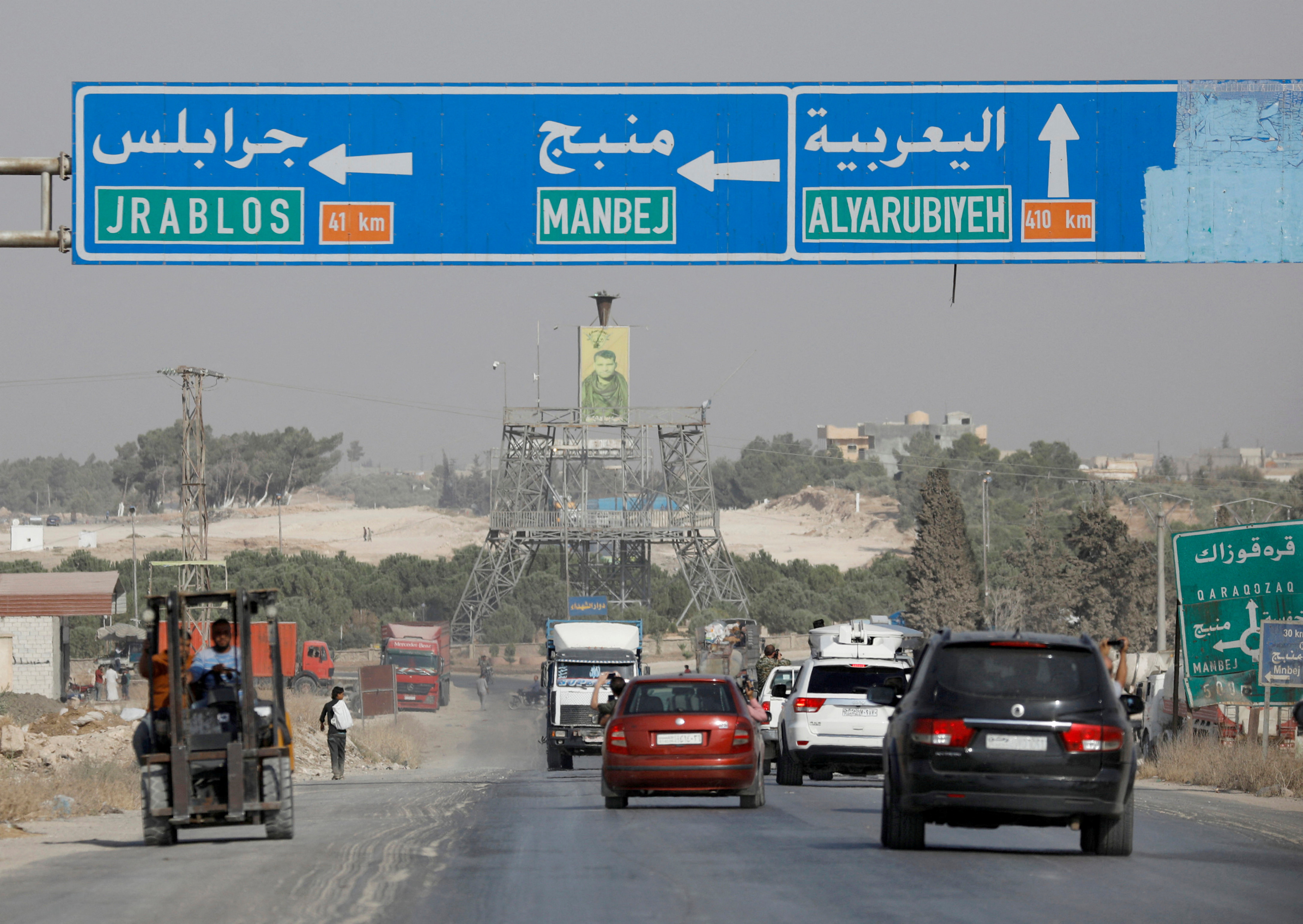 Cars pass under a road sign that shows the direction to Manbij city, at the entrance of Manbij