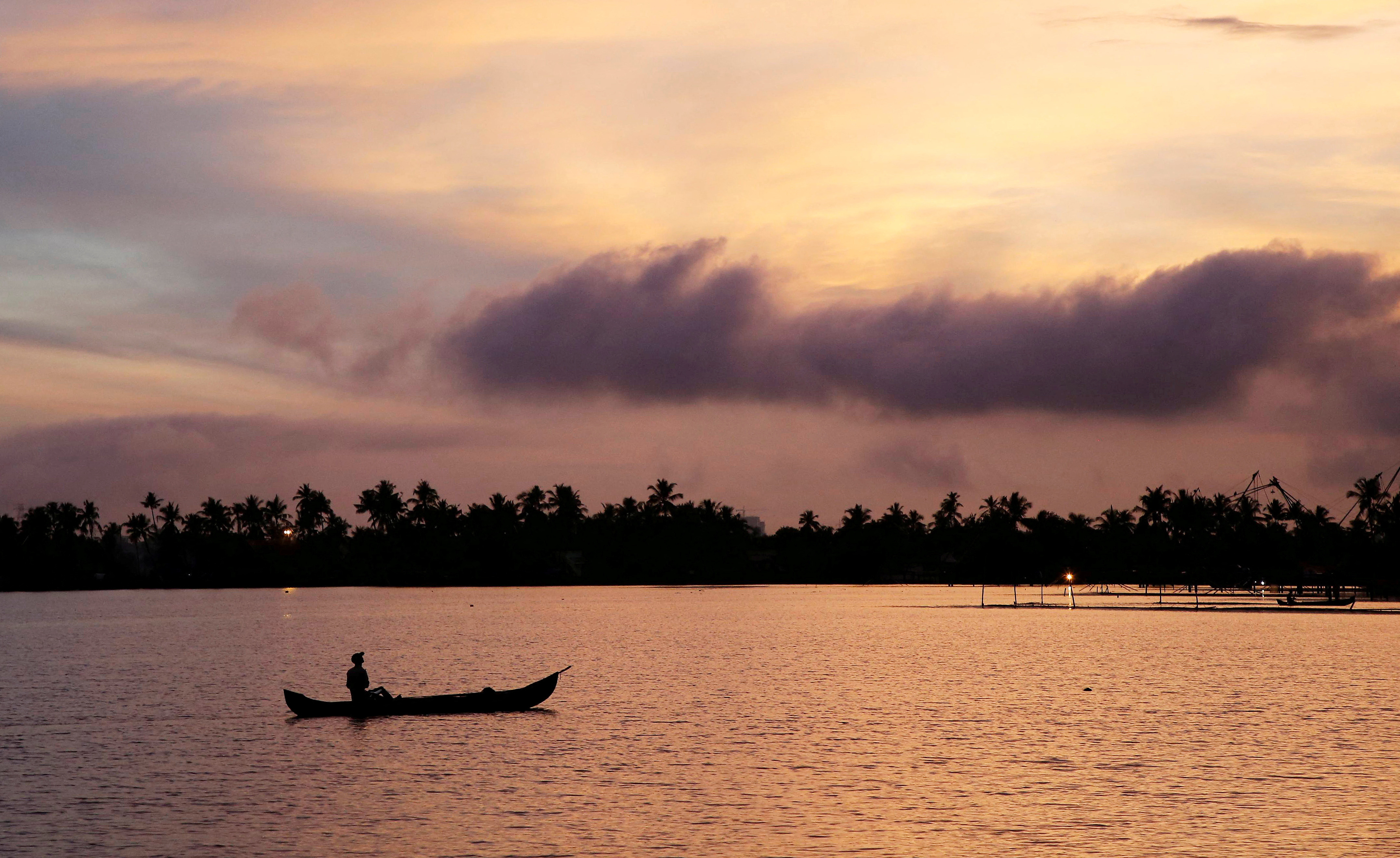 A man rows his boat in the tributary waters of Vembanad Lake against the backdrop of pre-monsoon clouds on the outskirts of Kochi