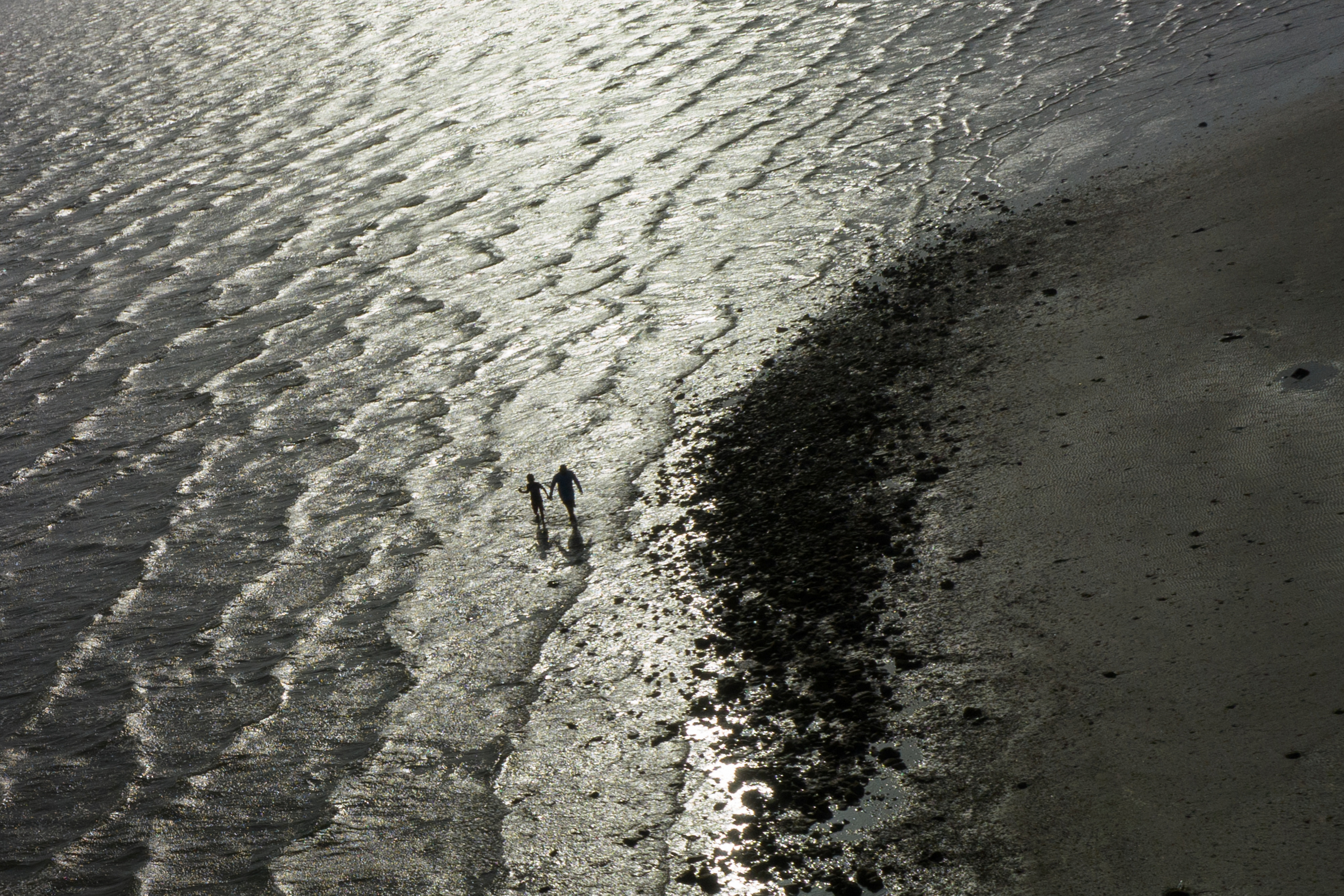 Father and child walk shoreline during hot weather in Texas City, Texas