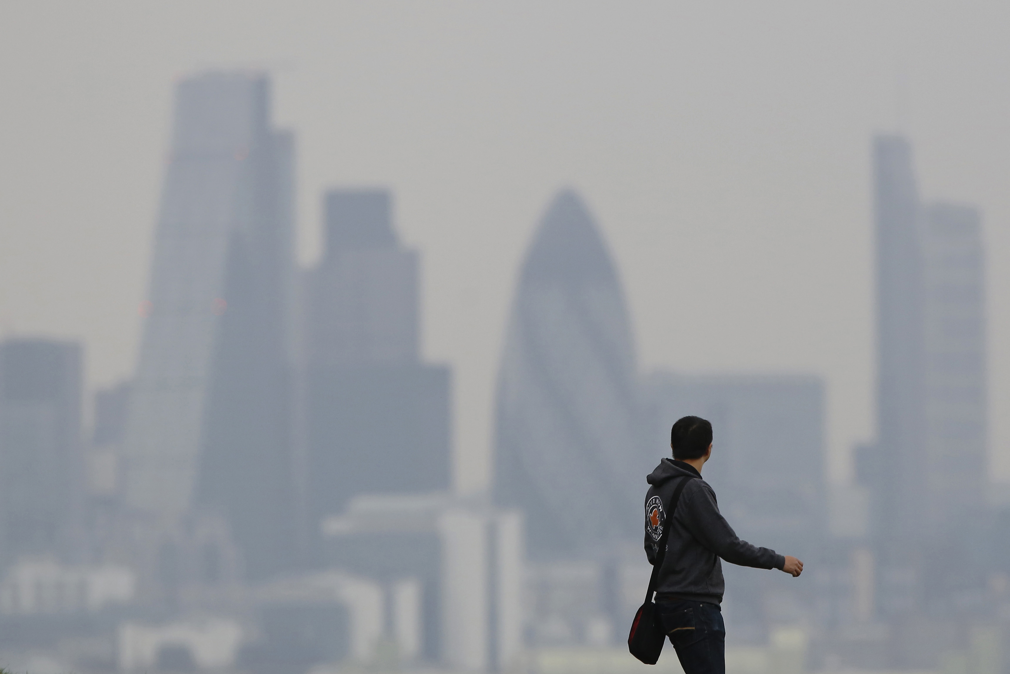 A man walks through Greenwich Park as a haze of pollution sits over the London skyline