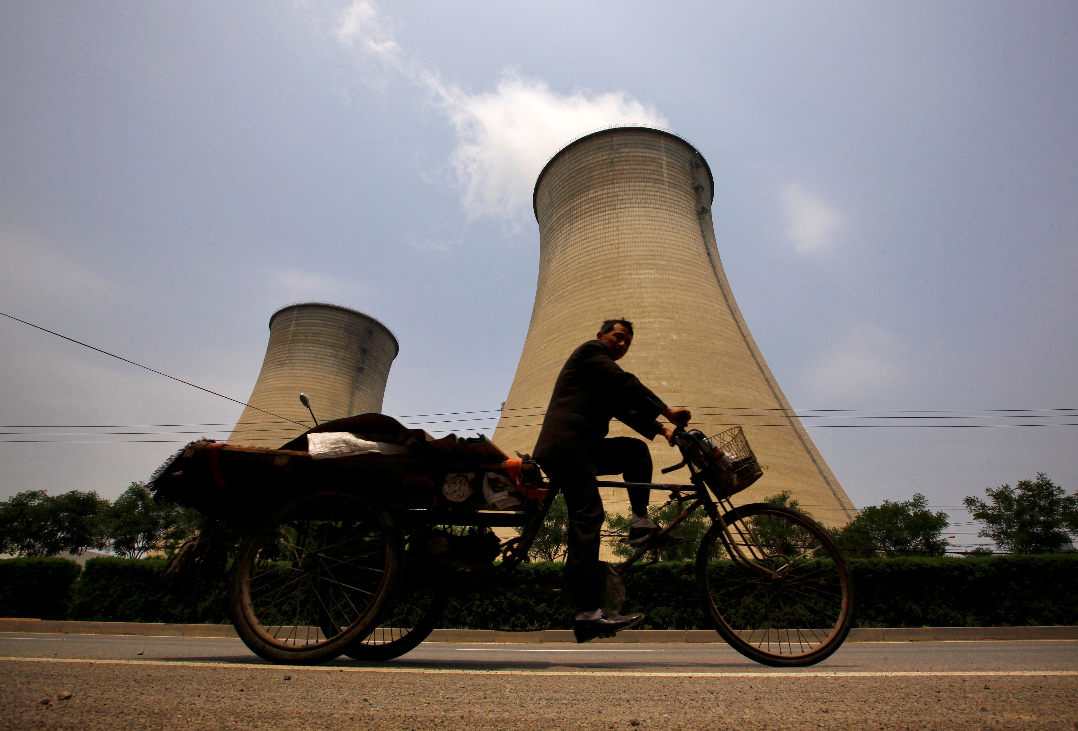 A man rides his tricycle past the cooling tower and chimneys from a coal-burning power station in Beijing