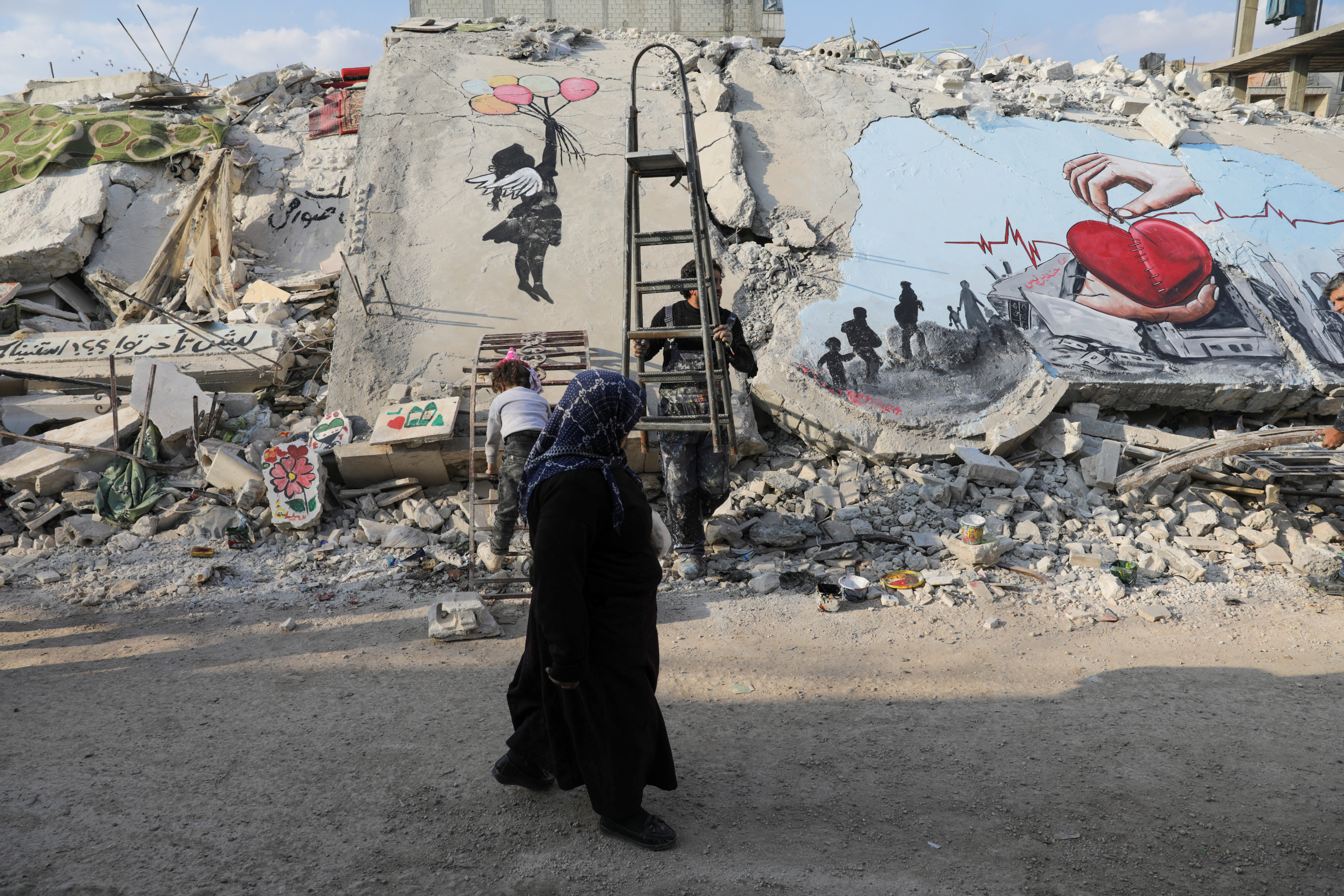 A woman walks past street art on rubble of damaged buildings in the rebel-held town of Jandaris