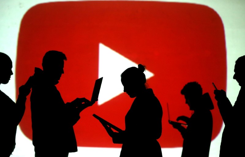 Silhouettes of laptop and mobile device users next to a screen projection of the YouTube logo in this picture illustration