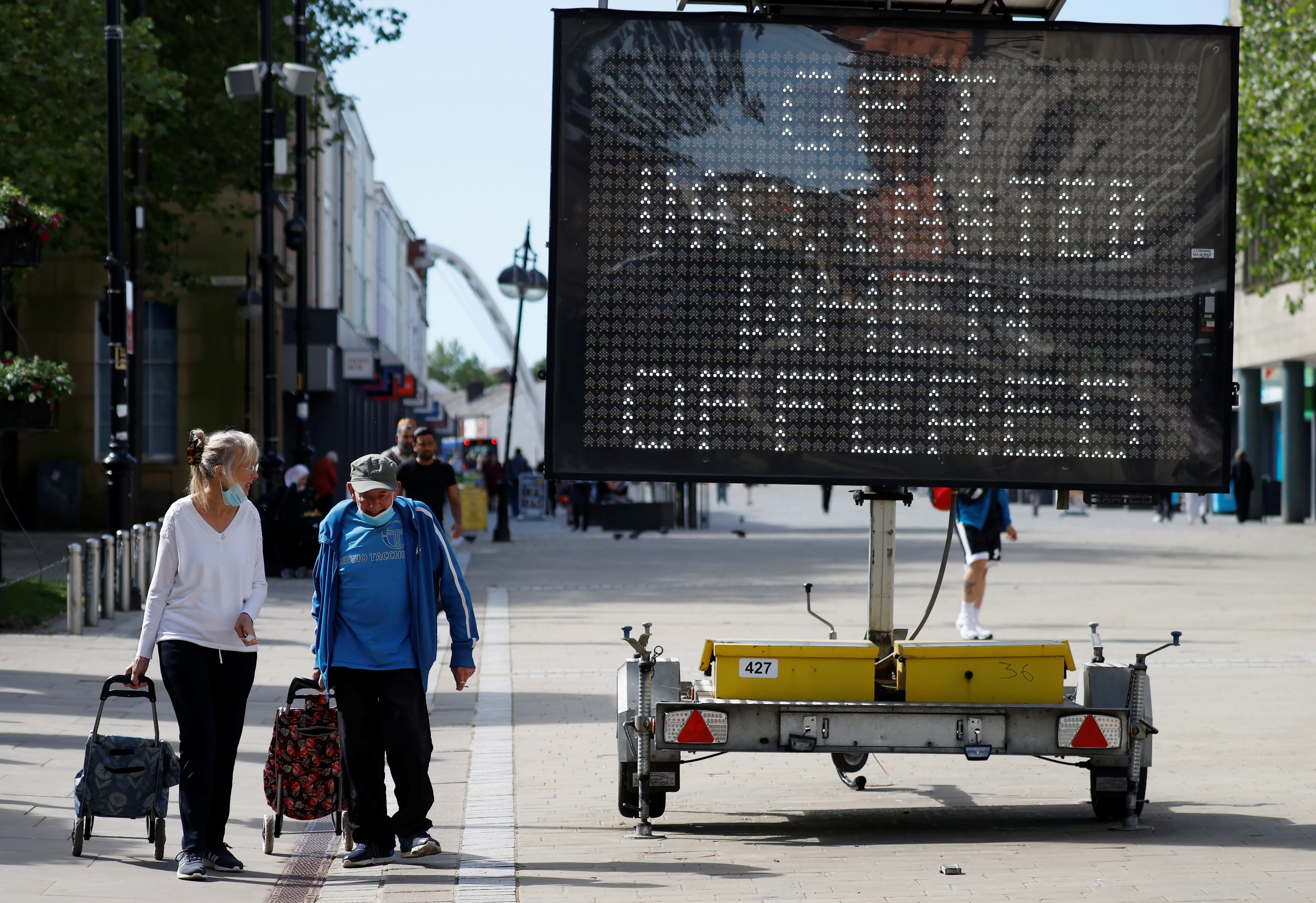 People pull shopping carts as they walk past an information board, amid the COVID-19 outbreak, in Bolton