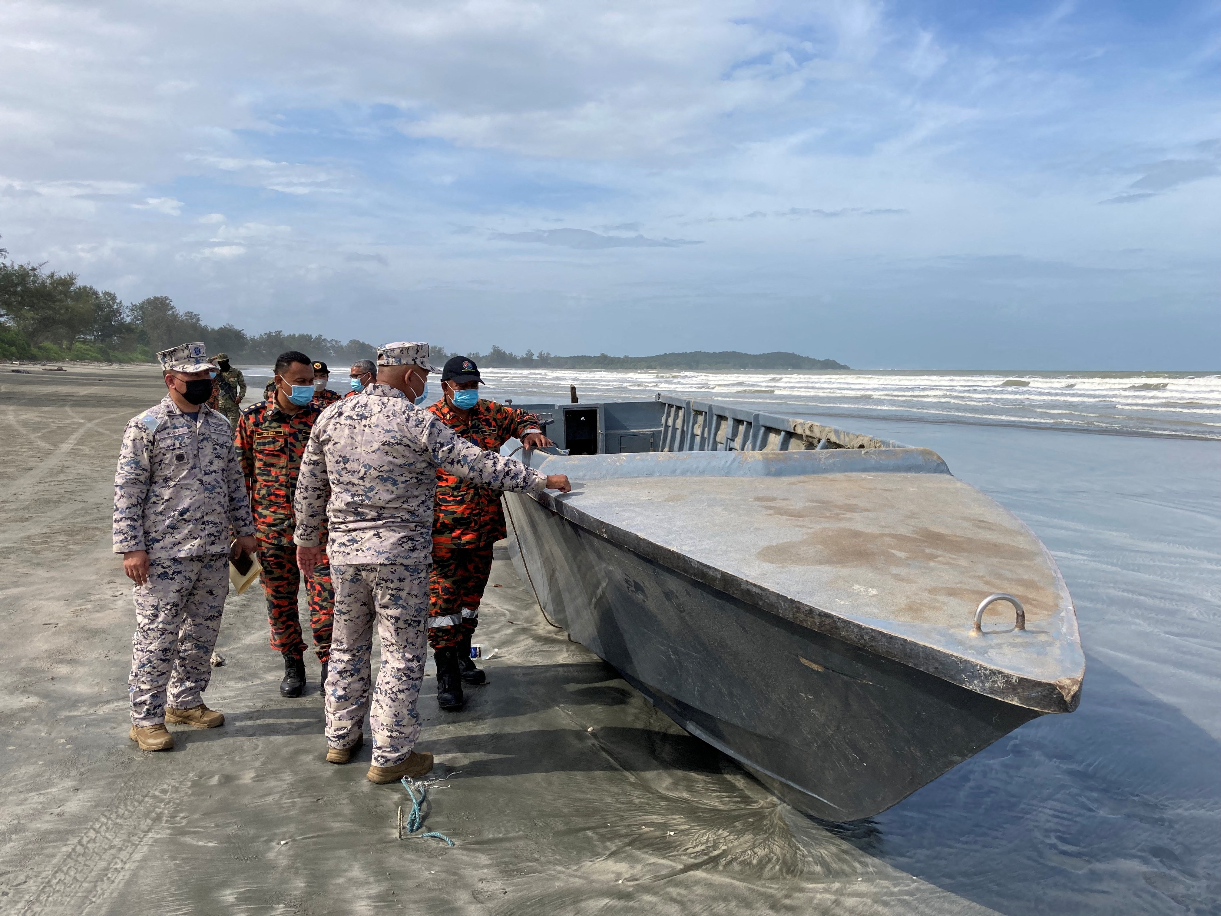Officials inspect a boat that capsized killing some of the people onboard while others remain missing in Kota Tinggi, Malaysia