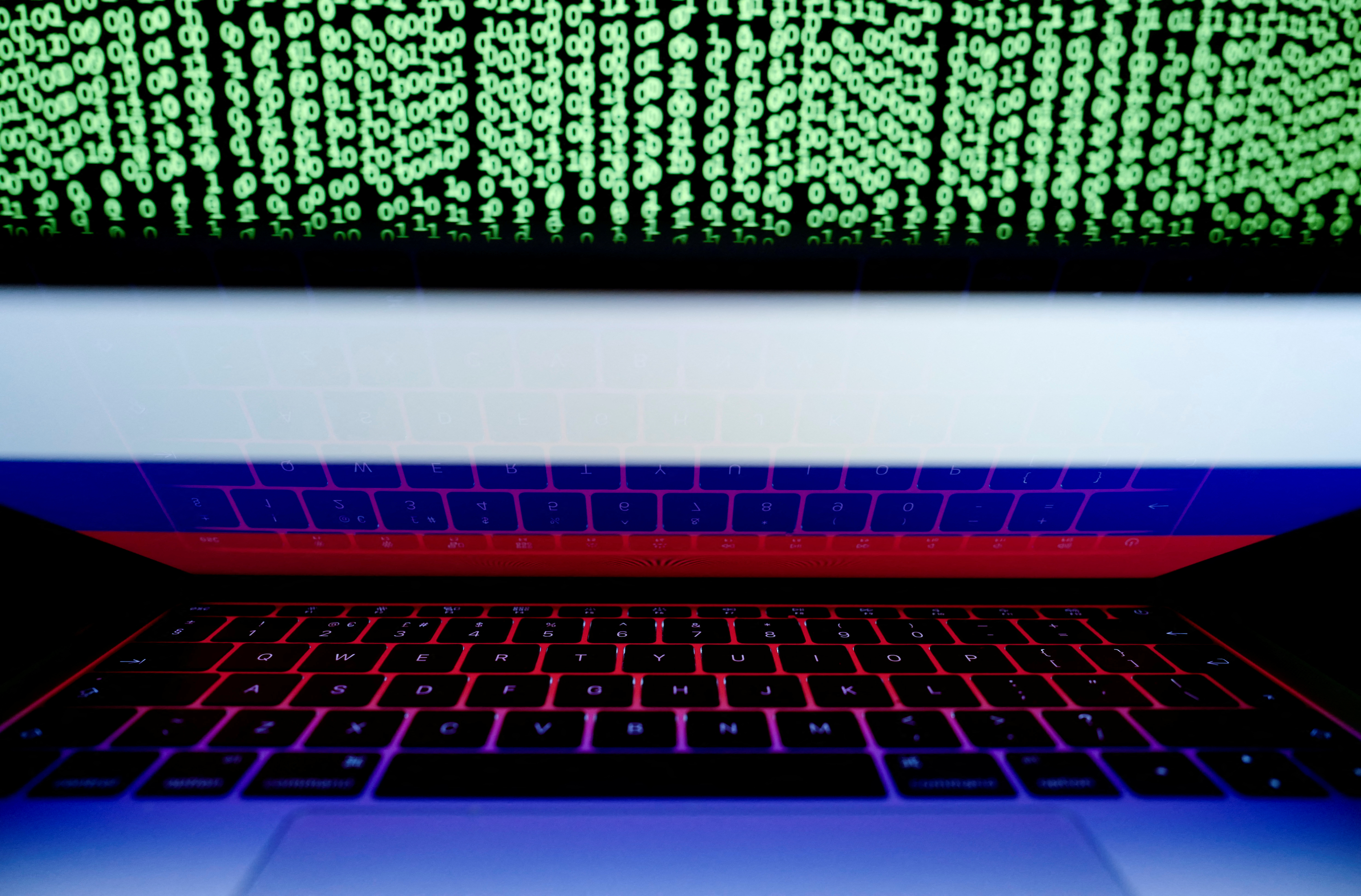 Russian flag is seen on the laptop screen in front of a computer screen on which cyber code is displayed, in this illustration picture