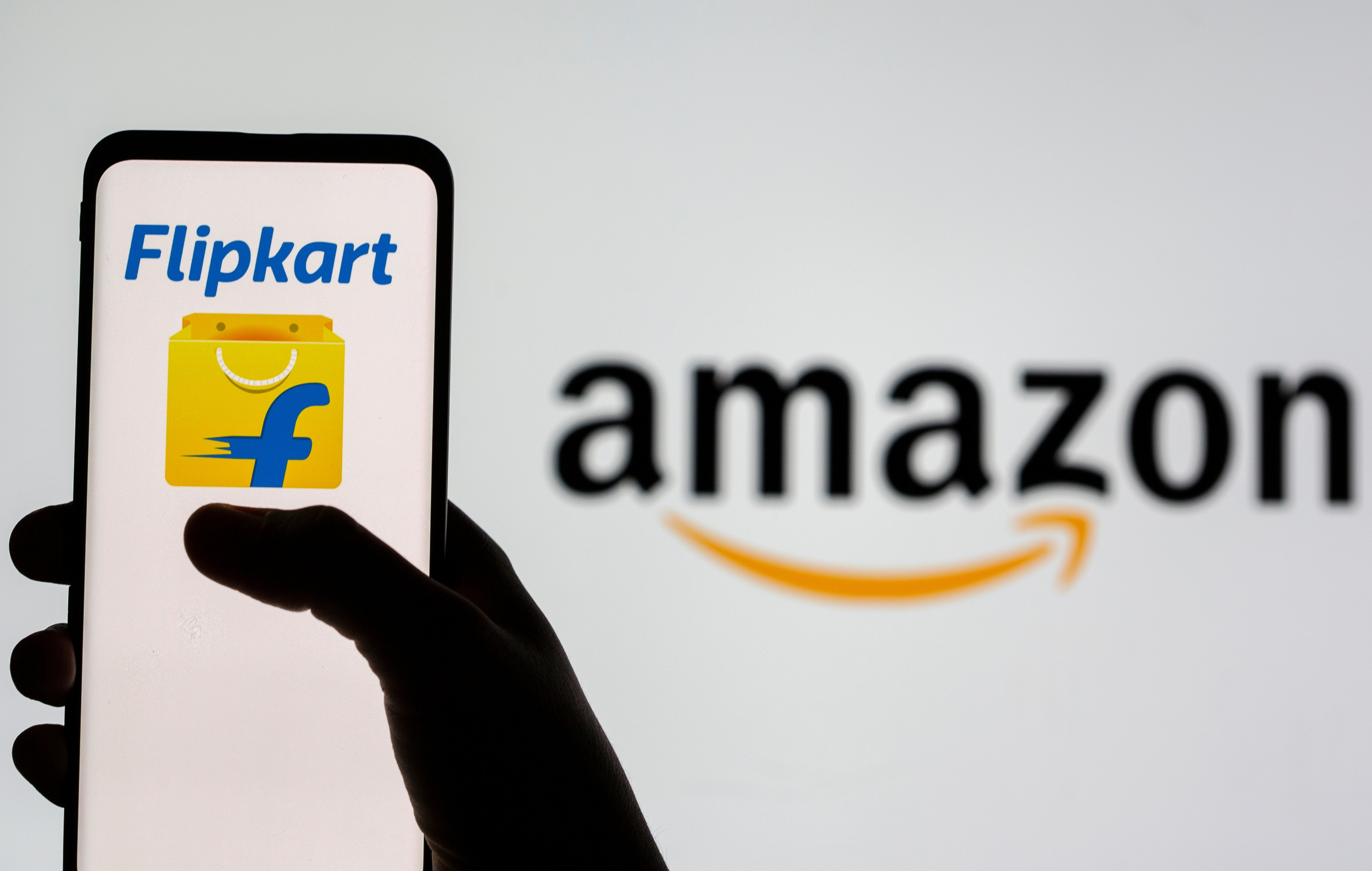 Smartphone with Flipkart logo is seen in front of displayed Amazon logo in this illustration taken