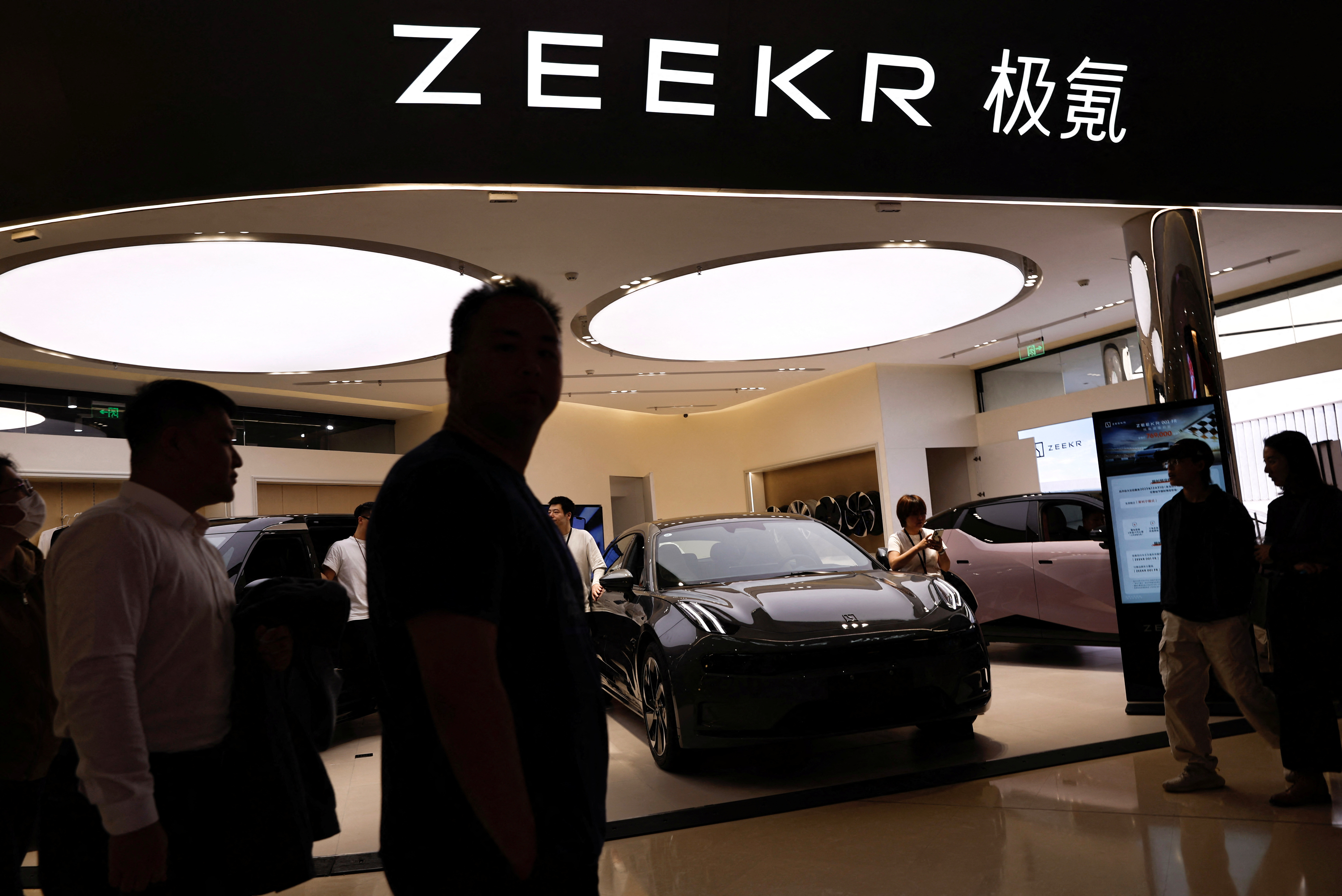 People walk past a booth of Zeekr, Chinese automaker Geely's premium electric vehicle (EV) brand, at a shopping mall in Beijing