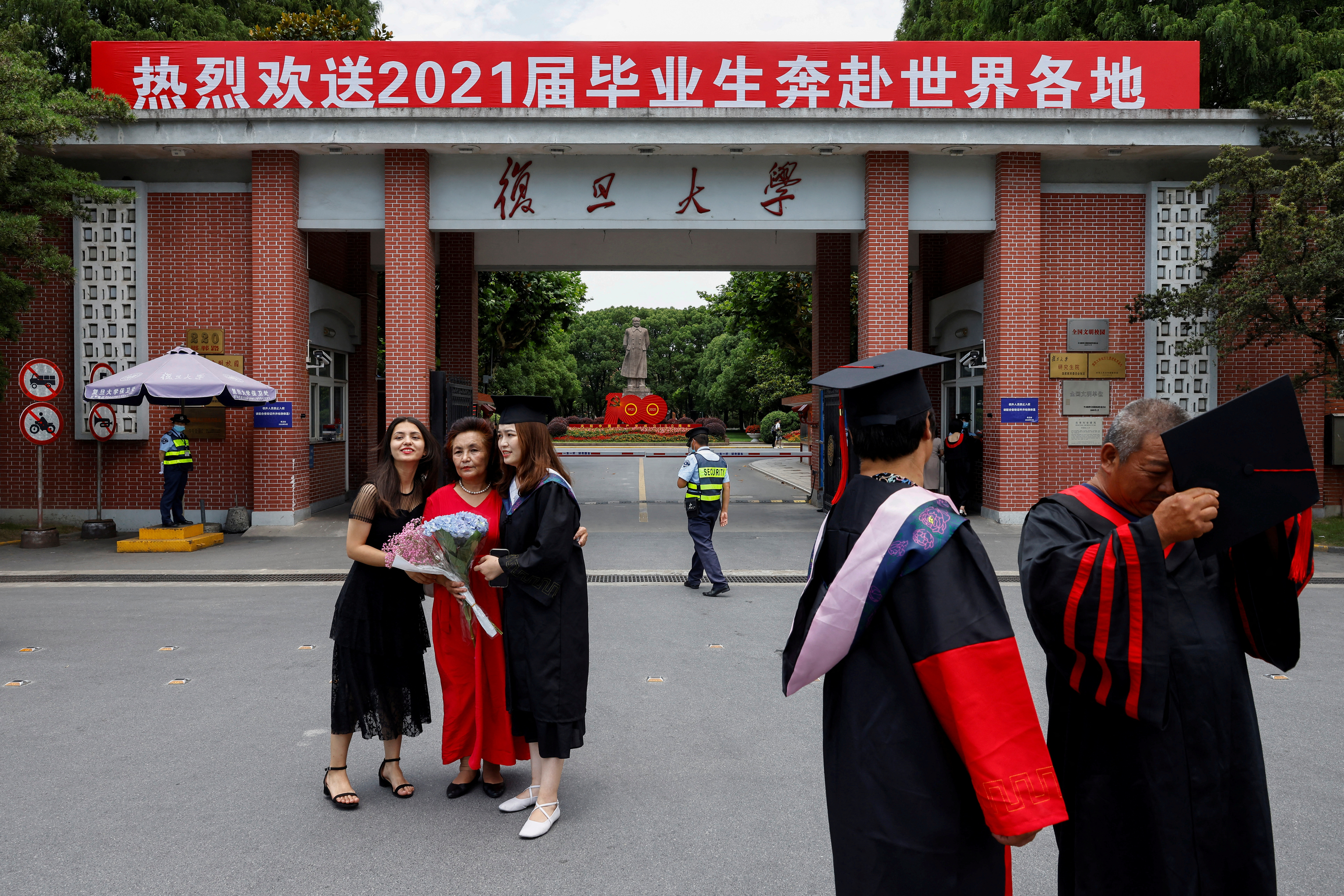 Students take graduation photo in front of the statue of Chinese leader Mao Zedong and a signboard marking the 100th founding anniversary of the Communist Party of China, at Fudan University in Shanghai