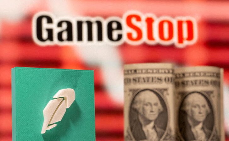 A 3d printed Robinhood logo and one dollar banknotes are seen in front of displayed GameStop logo
