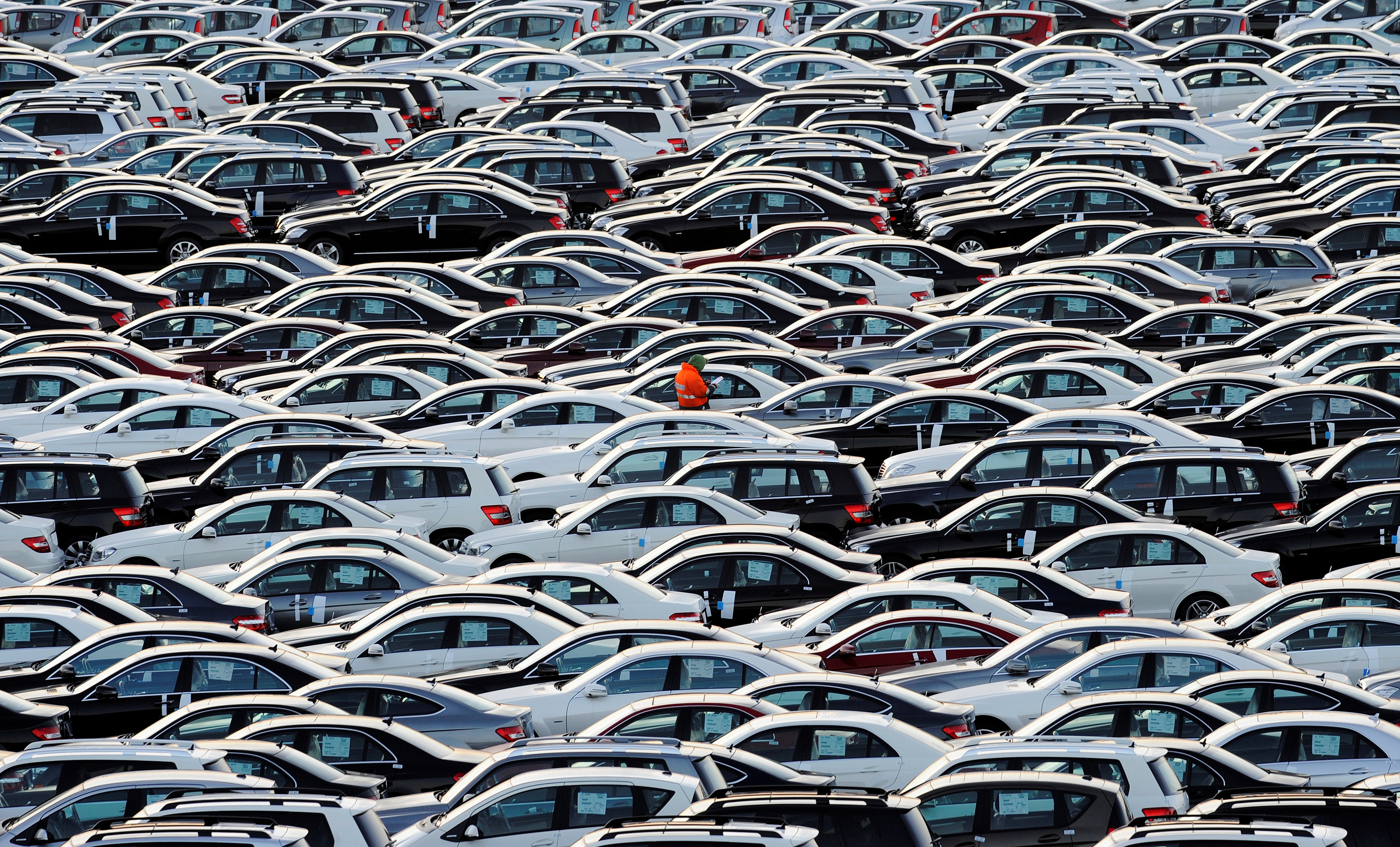 A worker walks along rolls of Mercedes cars at a shipping terminal in the harbor of the town of Bremerhaven