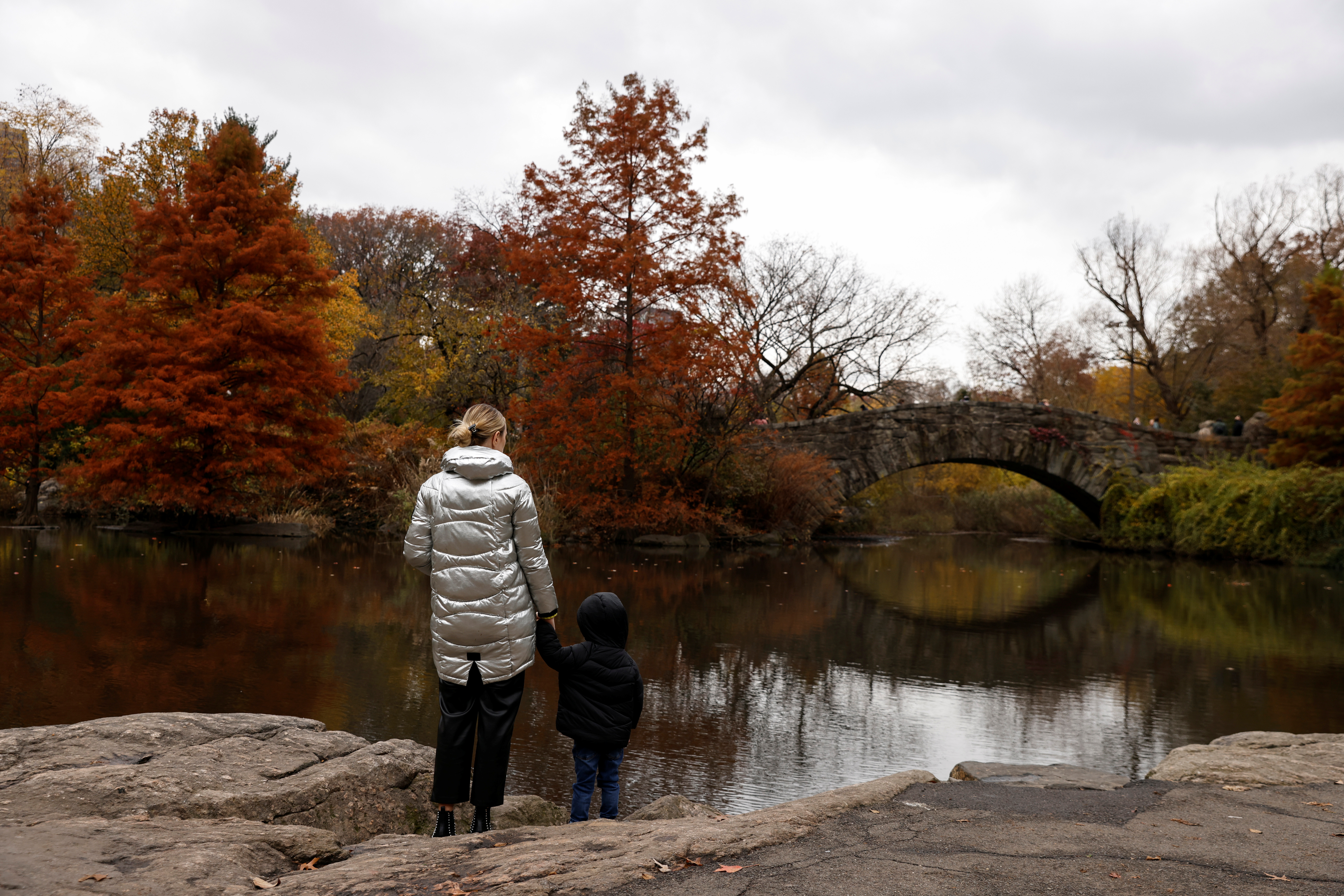A woman holds the hand of a child by a pond at Central Park in New York City