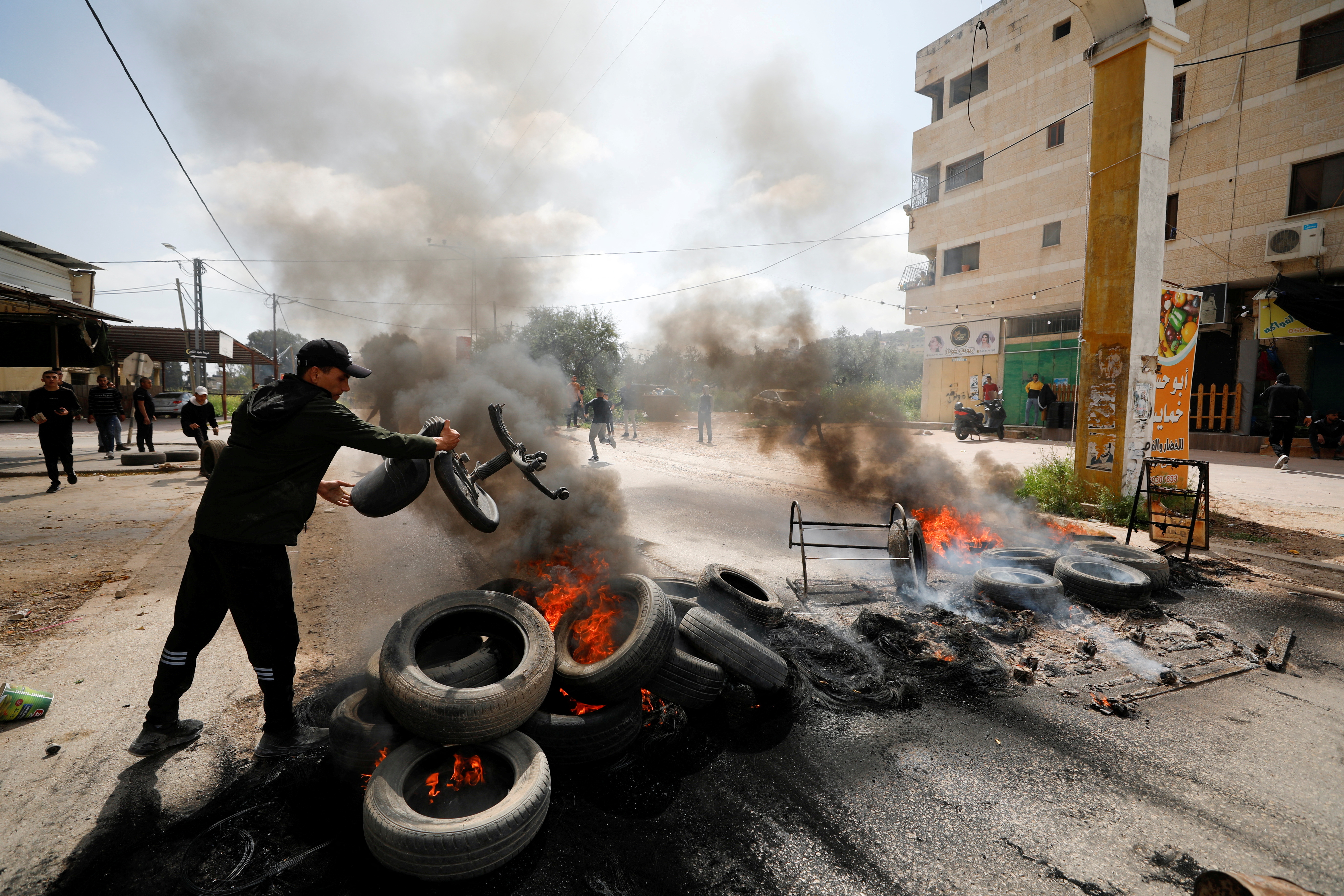 A Palestinian throws a chair at burning tires during clashes with Israeli forces following a raid, in Jenin in the Israeli-occupied West Bank