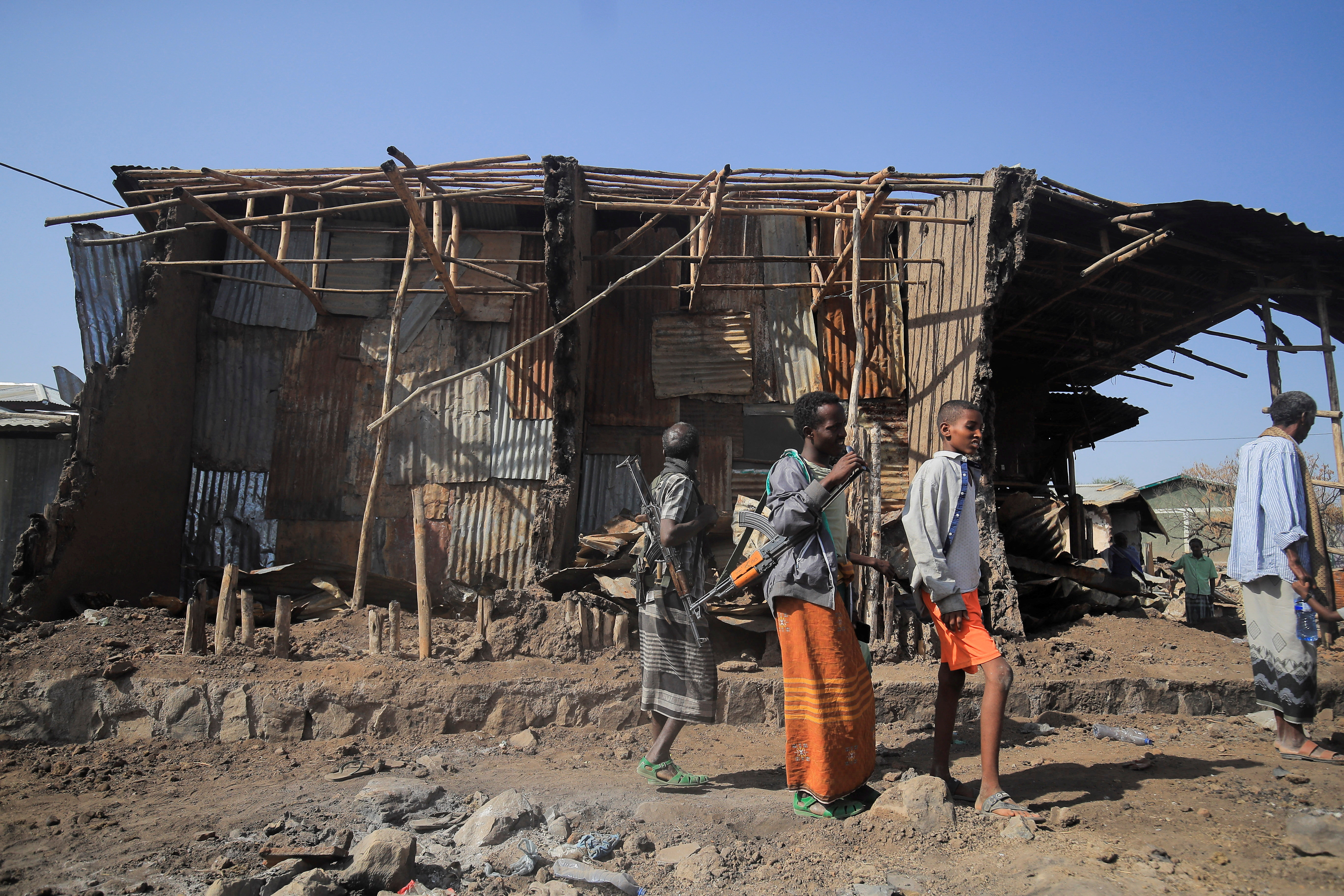 Residents and militias stand next to houses destroyed by an airstrike in Kasagita town