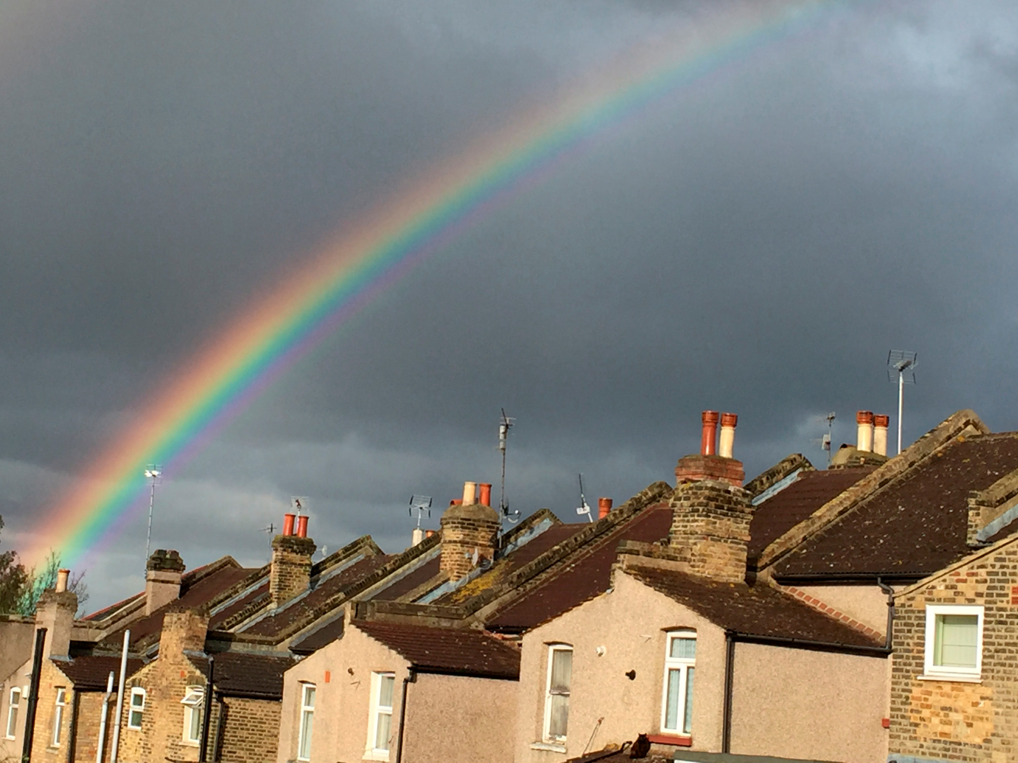 A rainbow forms over terraced housing during a rain storm in south London