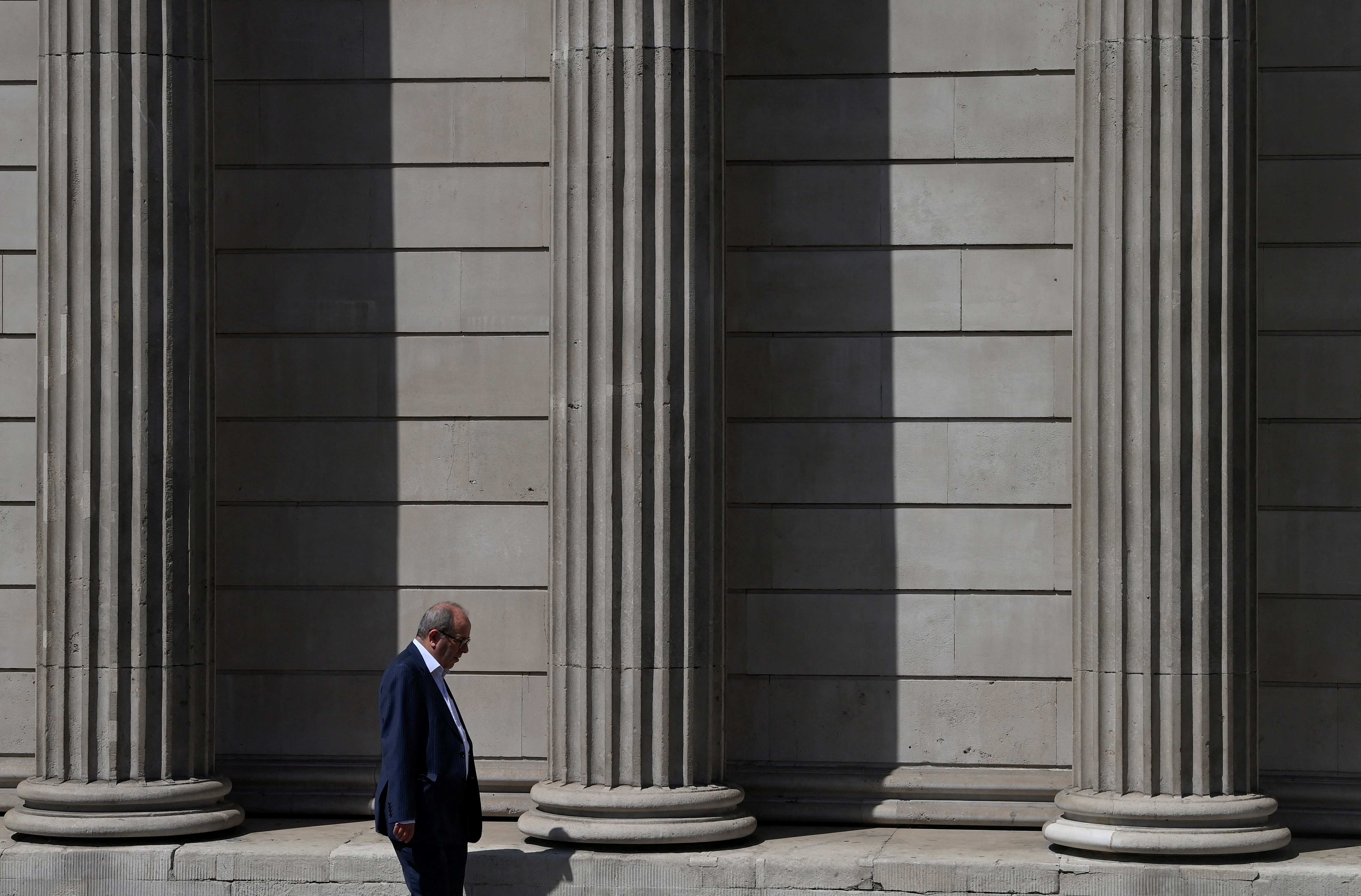 A worker walks past the Bank of England during the hot weather in the City of London financial district, London