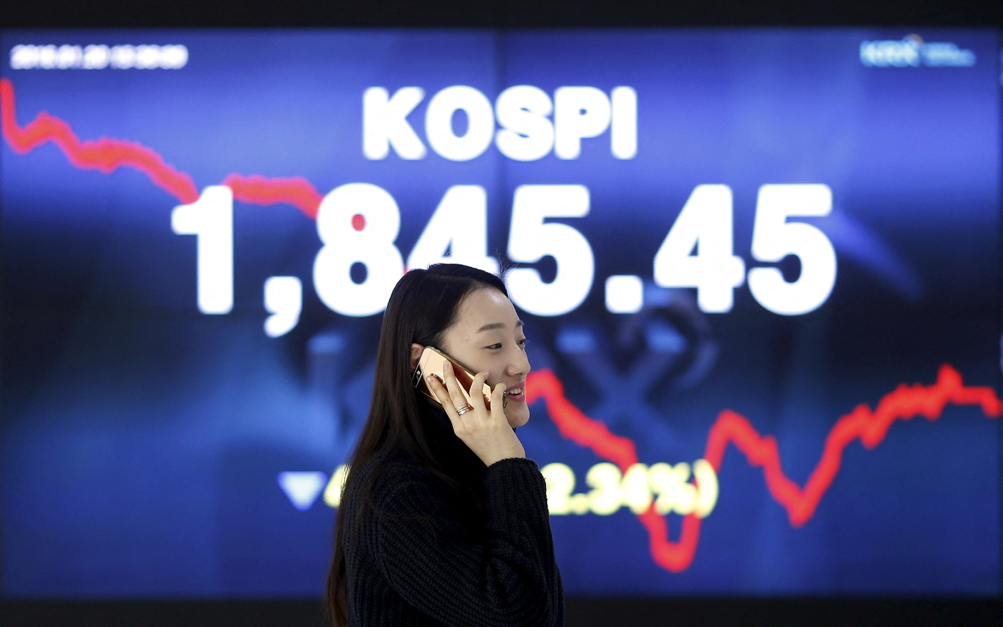 Woman walks past electronic board KOSPI at the Korea Exchange in Seoul