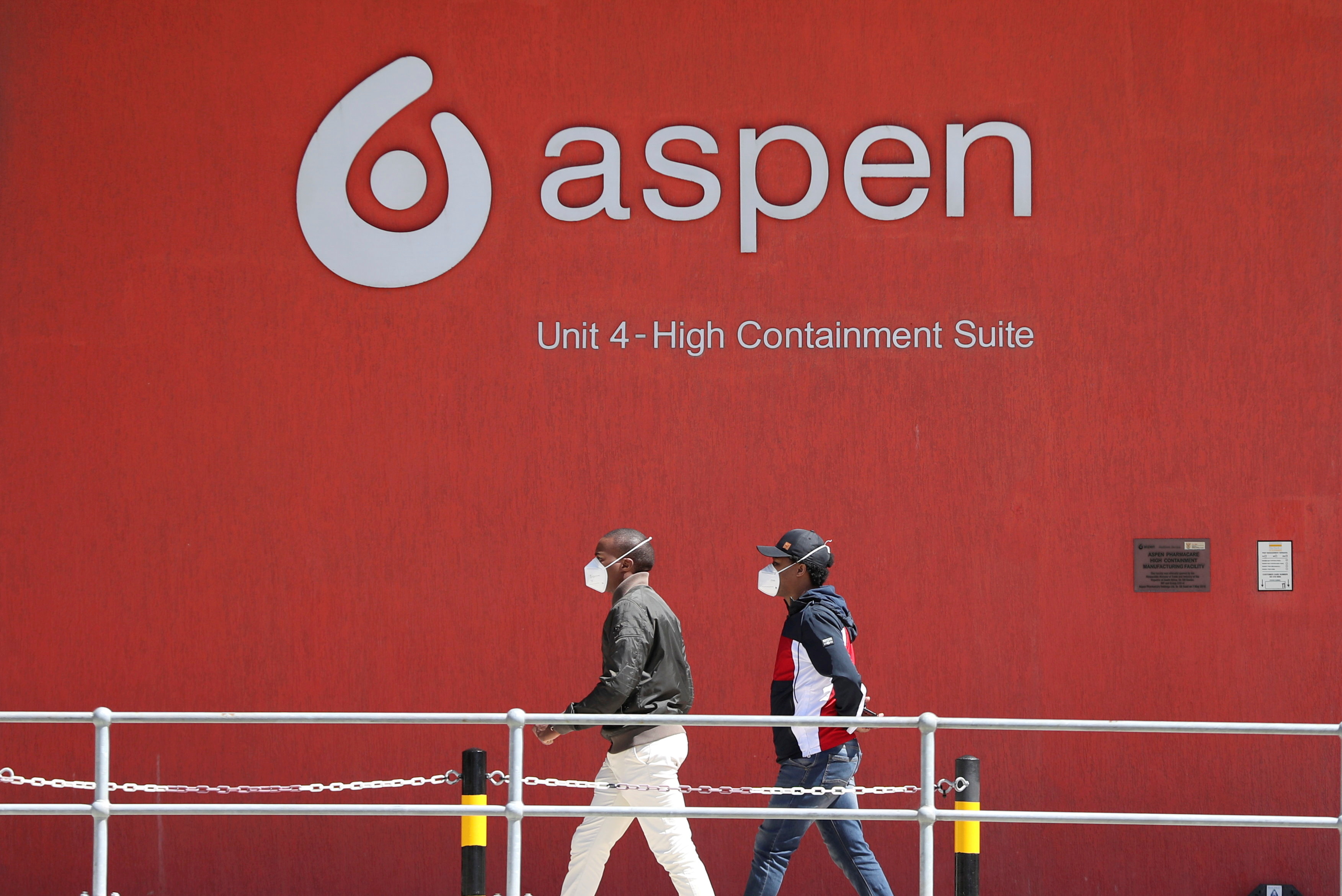 People wearing face masks walk past a logo of South African pharmaceuticals company Aspen Pharmacare at its Johnson & Johnson COVID-19 vaccine facility in Gqeberha, South Africa