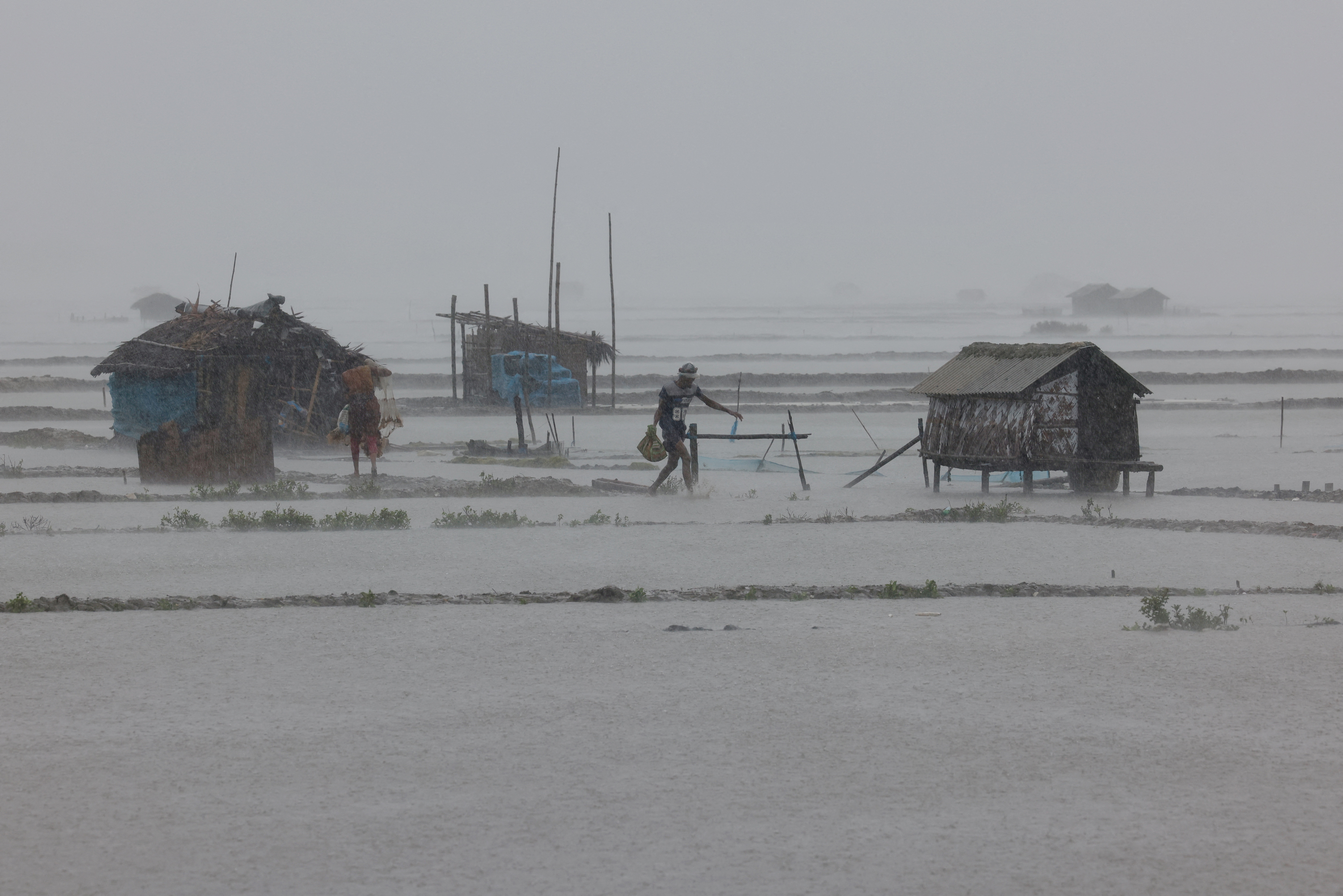 People walk along flooded shrimp and crab farms due to heavy rain as Cyclone Remal passes the country in the Shyamnagar area of Satkhira