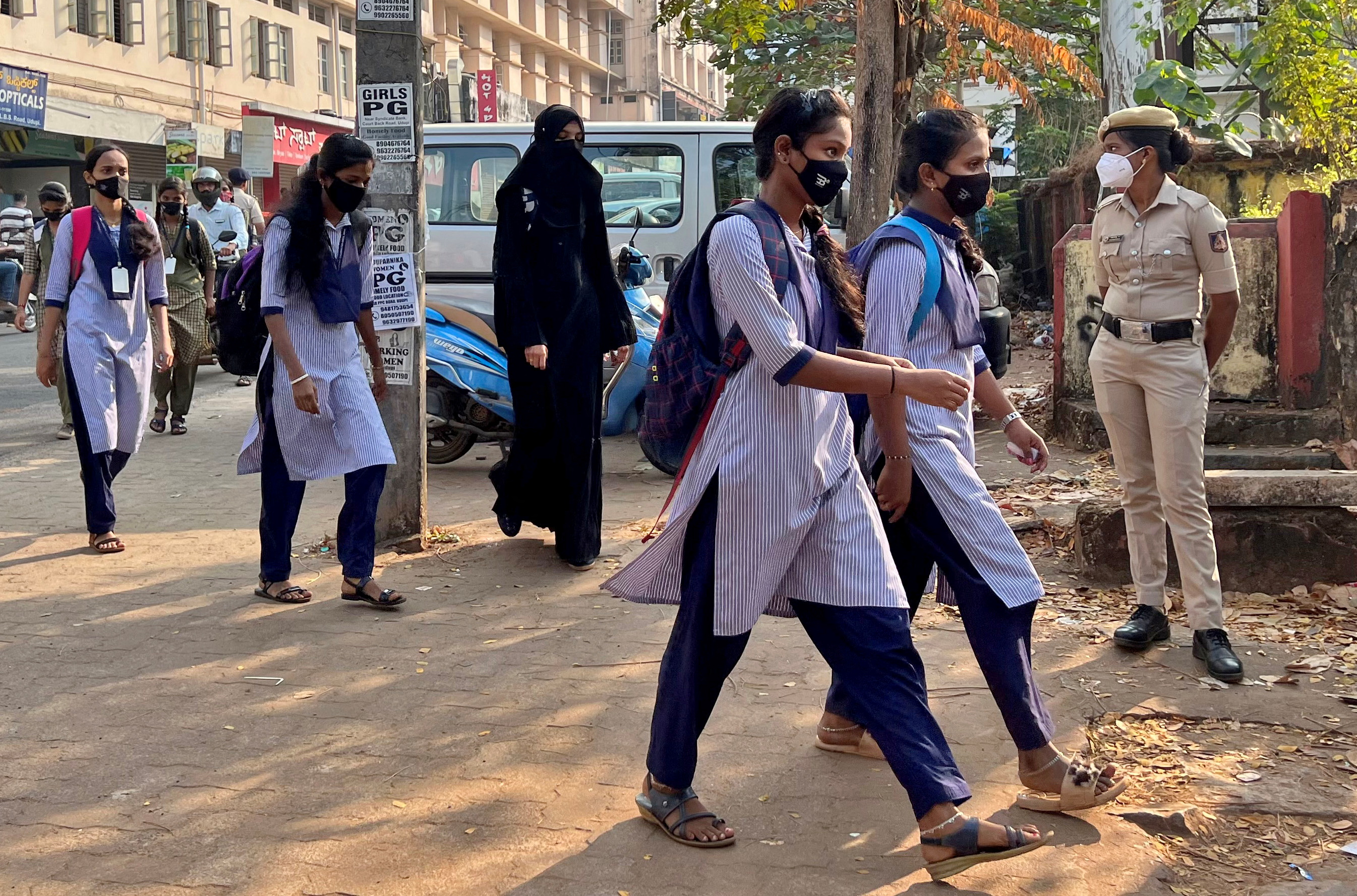 Des écolières arrivent pour assister à leurs cours tandis qu'une policière garde devant une école gouvernementale pour filles après la récente interdiction du hijab, dans la ville d'Udupi, dans l'État méridional du Karnataka, en Inde, le 16 février 2022. REUTERS/Sunil Kataria
