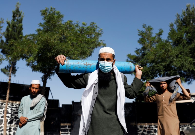 A man waits outside a factory to get his oxygen cylinder refilled as he holds it on his shoulder, in Kabul