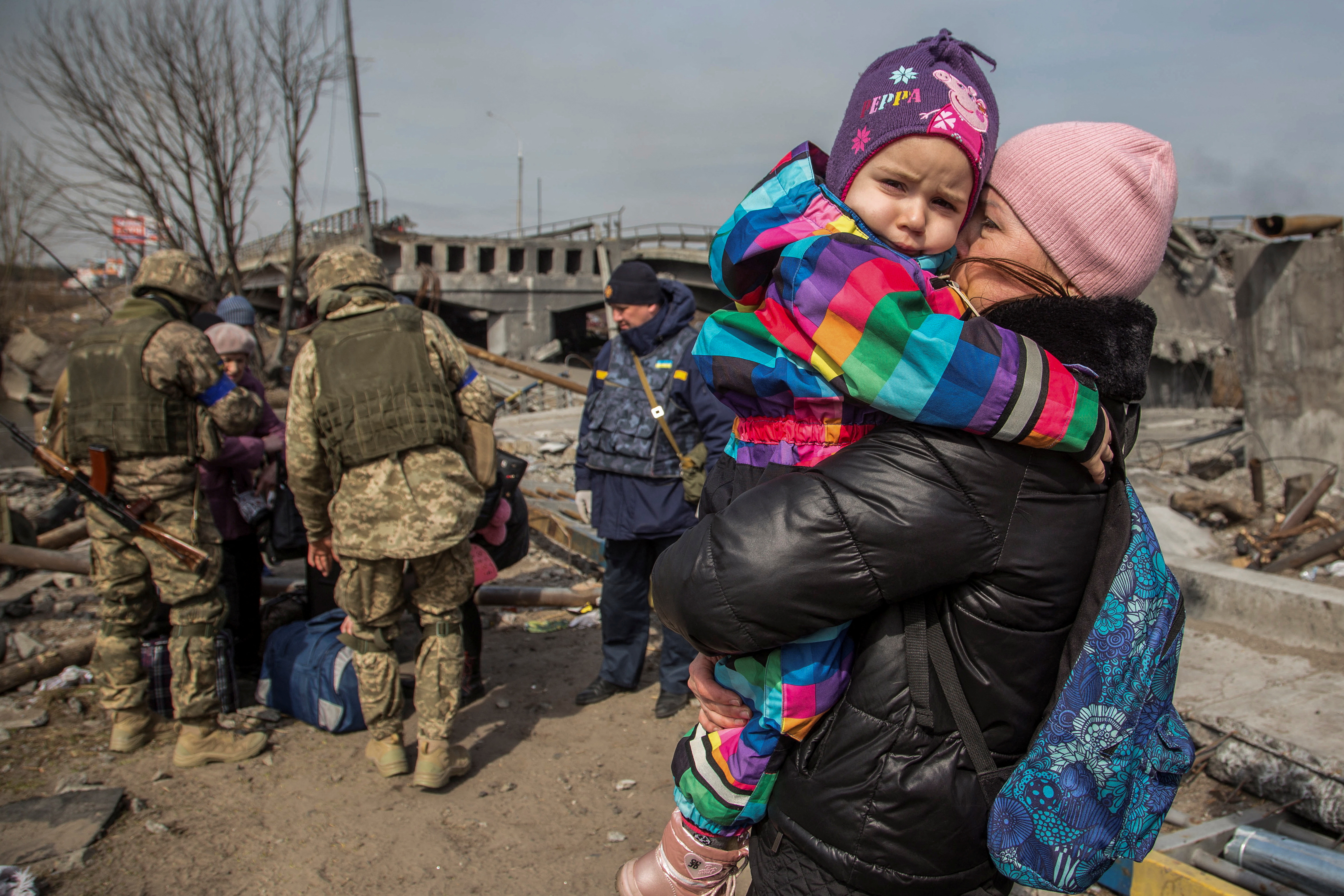 A woman holds a child next to a destroyed bridge during evacuation from the town of Irpin