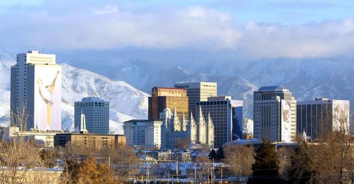 The downtown buildings of Salt Lake City glow in the setting sun with the Wasatch mountain range loo..