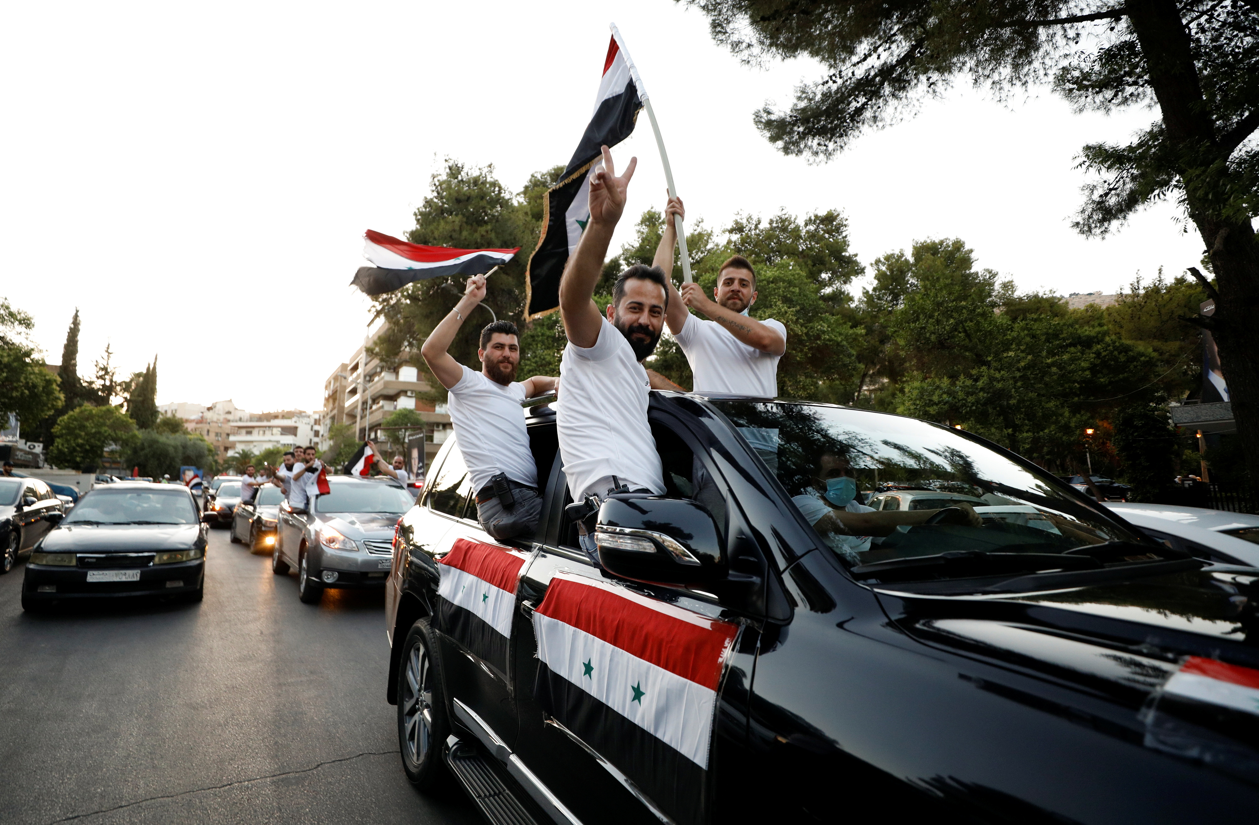 People gesture and hold Syrian national flags from a car during the country's presidential elections in Damascus