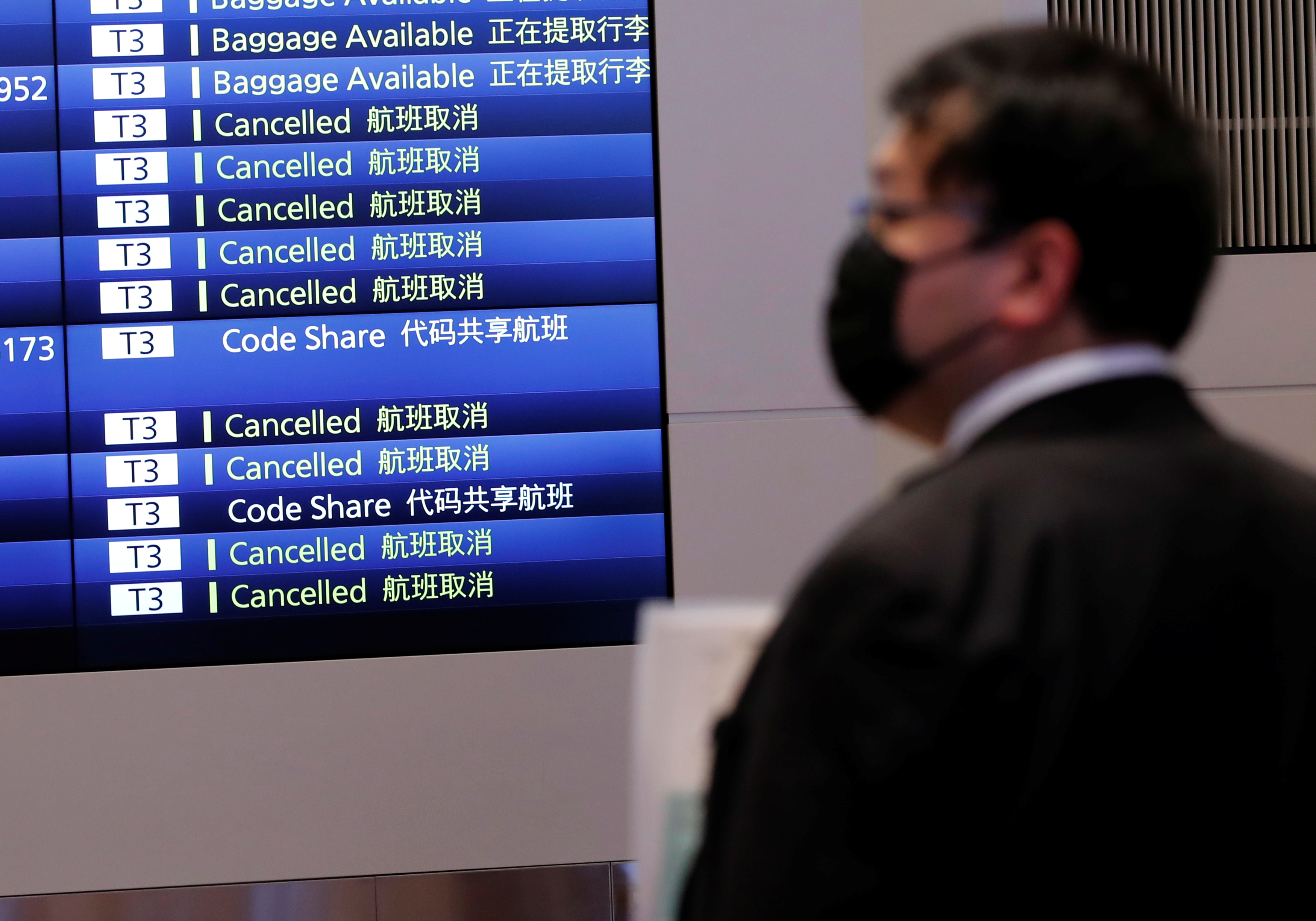 A man stands in front of a monitor showing flight schedules at an arrival hall of Haneda airport's international terminal, amid the coronavirus disease (COVID-19) outbreak, in Tokyo