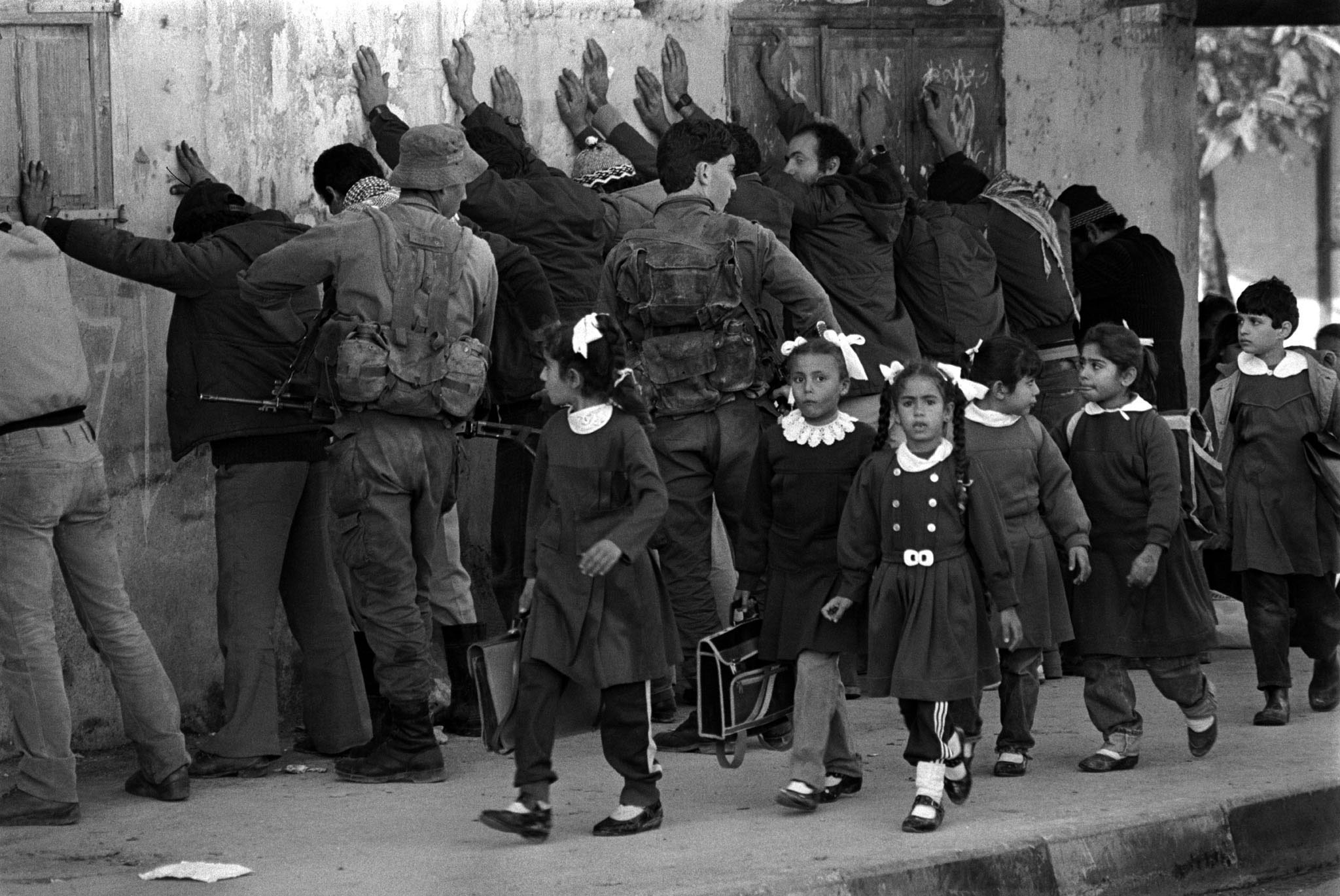 Palestinian school girls returning home from classes pass a line of Arab men being frisked by Israeli soldiers in the Gaza Strip in 1986 after a Jewish man was stabbed and seriously injured.  REUTERS